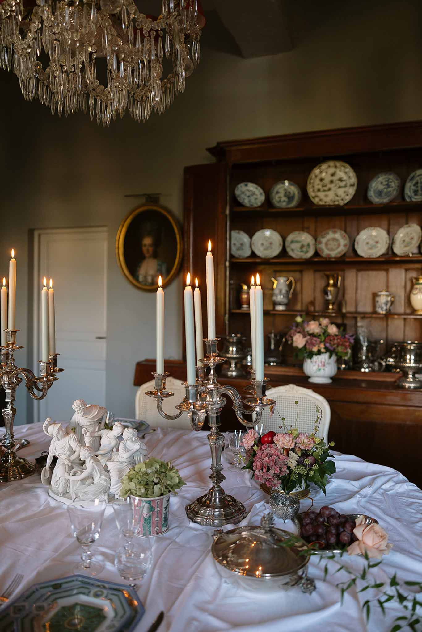 Chateau dining room with silver candelabras, pink roses, crystal chandelier, and blue-white transferware display