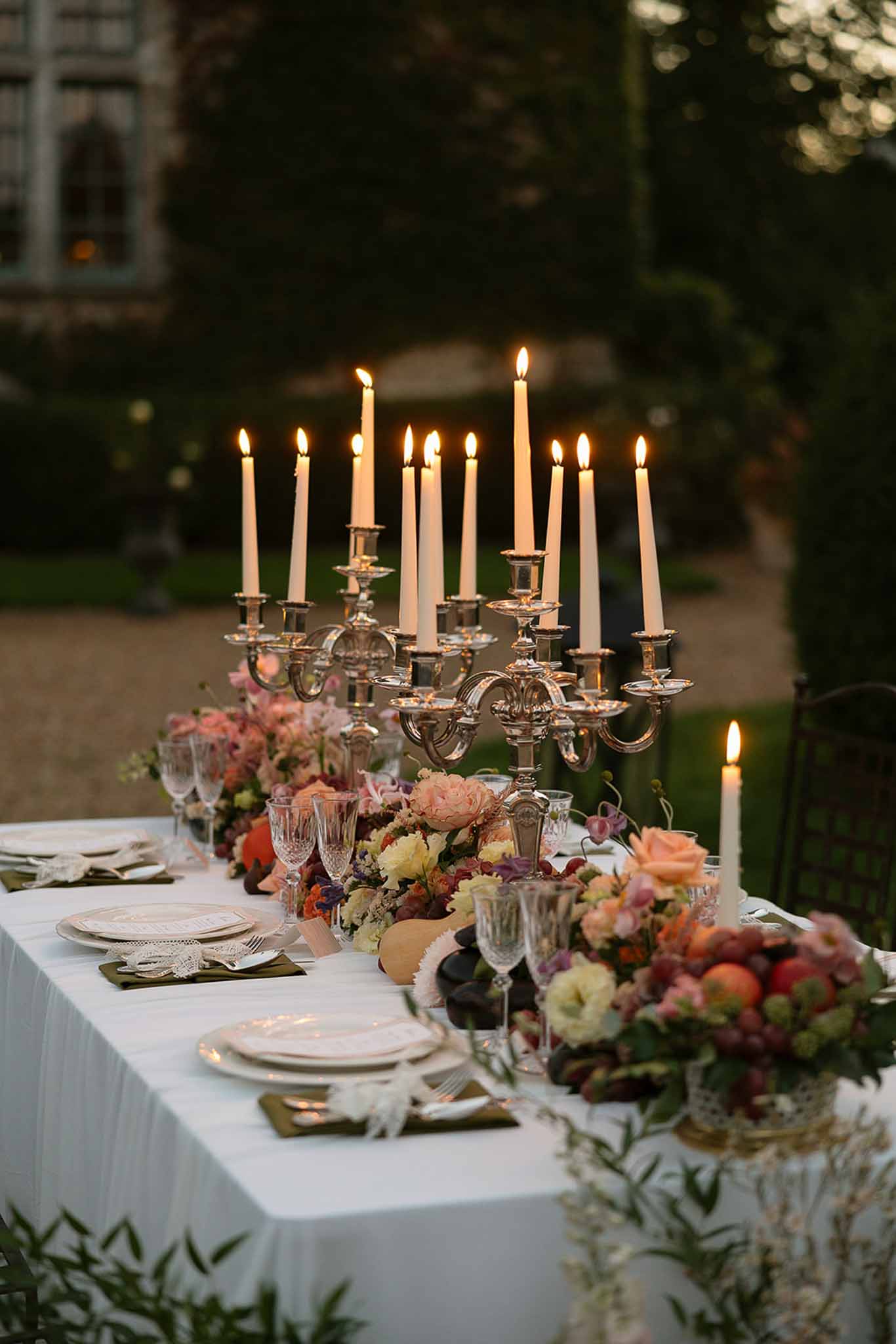 Silver candelabra table with peach rose, burgundy dahlia, and grape baroque runner beside olive napkins at dusk