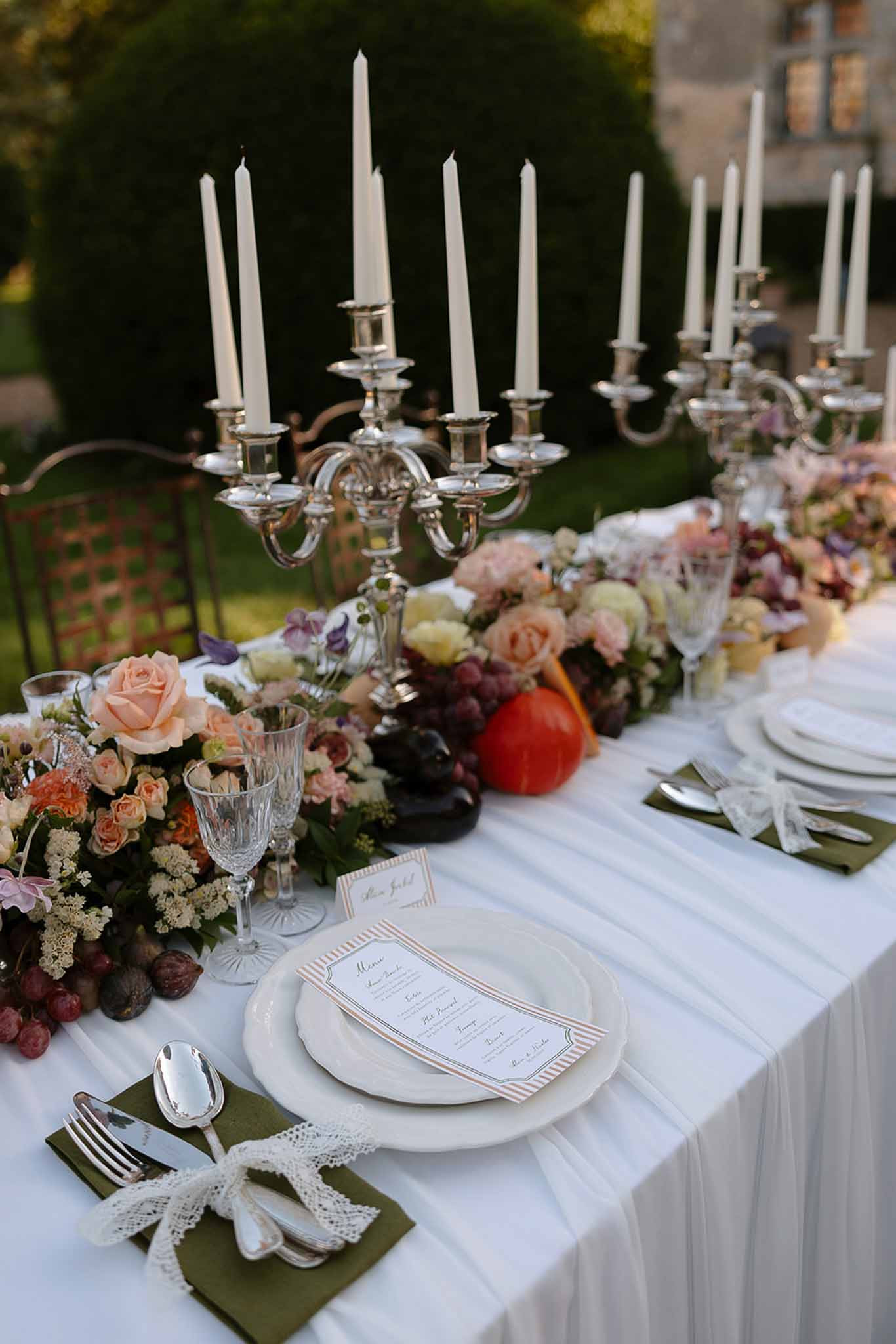 Autumn harvest tablescape with peach roses, figs, grapes, silver candelabras, and olive napkins
