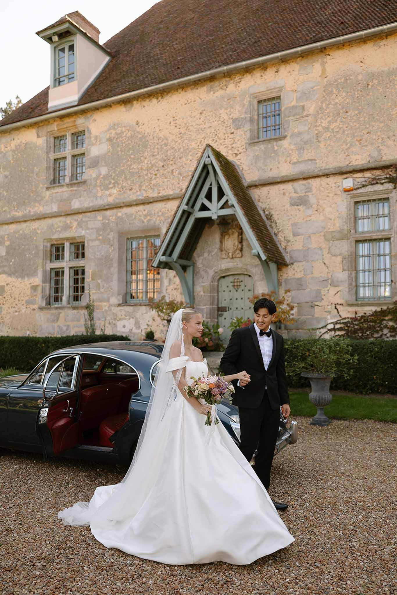 Bride and groom by vintage green car with red interior, bride holding mixed pastel bouquet