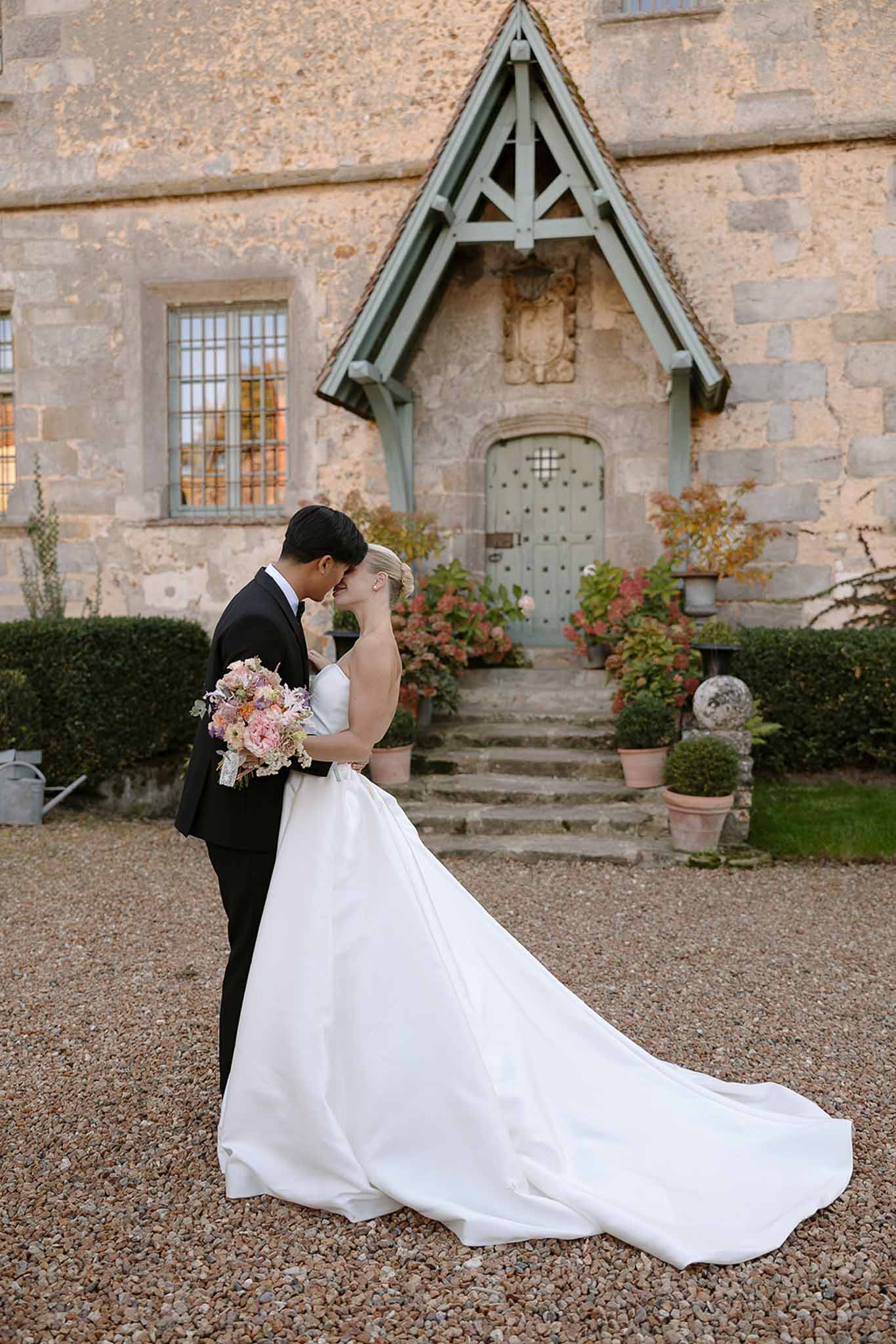 Bride and groom forehead-to-forehead at chateau entrance, bride in white ballgown with cathedral train and blush bouquet