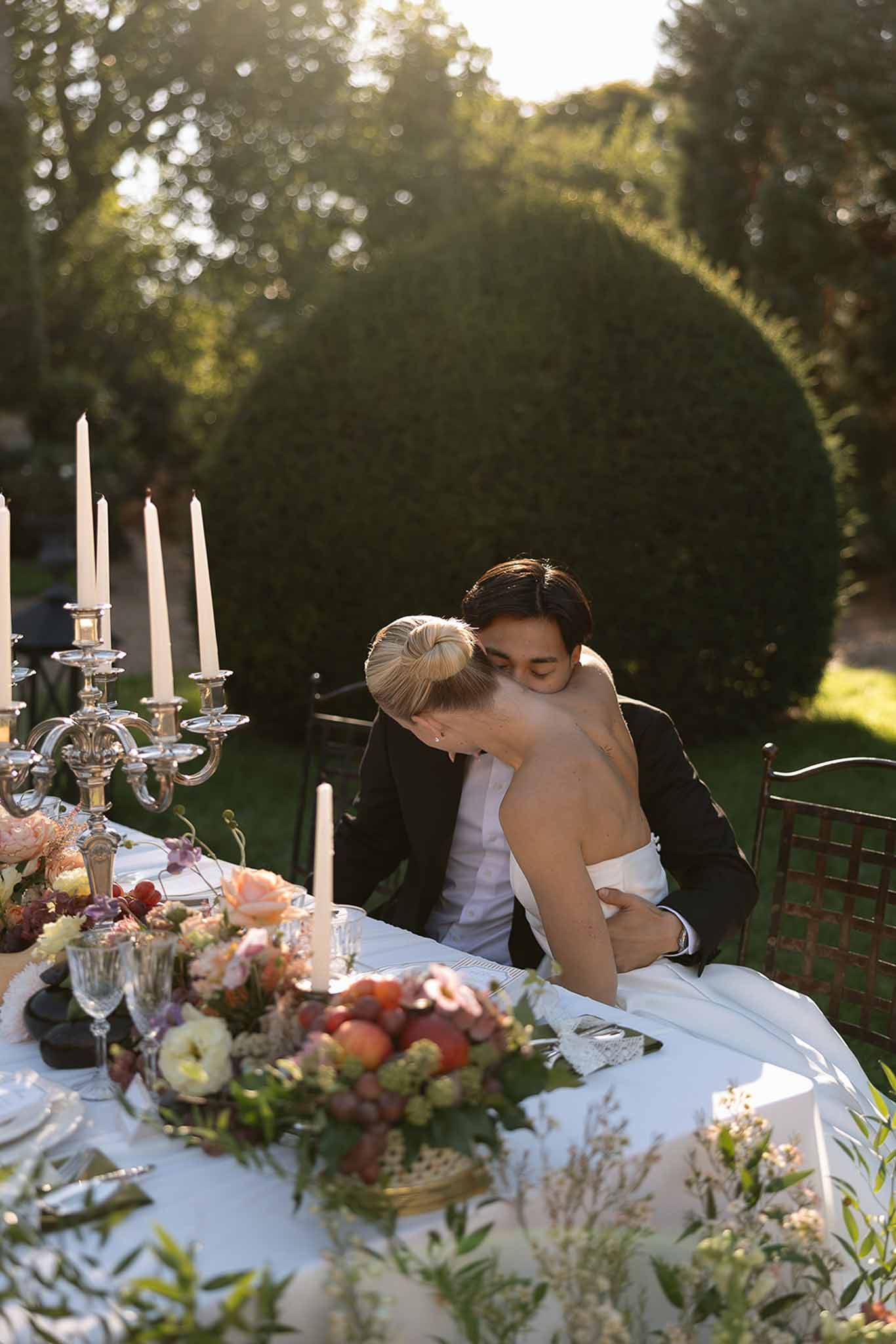 Bride and groom embracing at sweetheart table with lush floral centerpieces in an outdoor garden reception