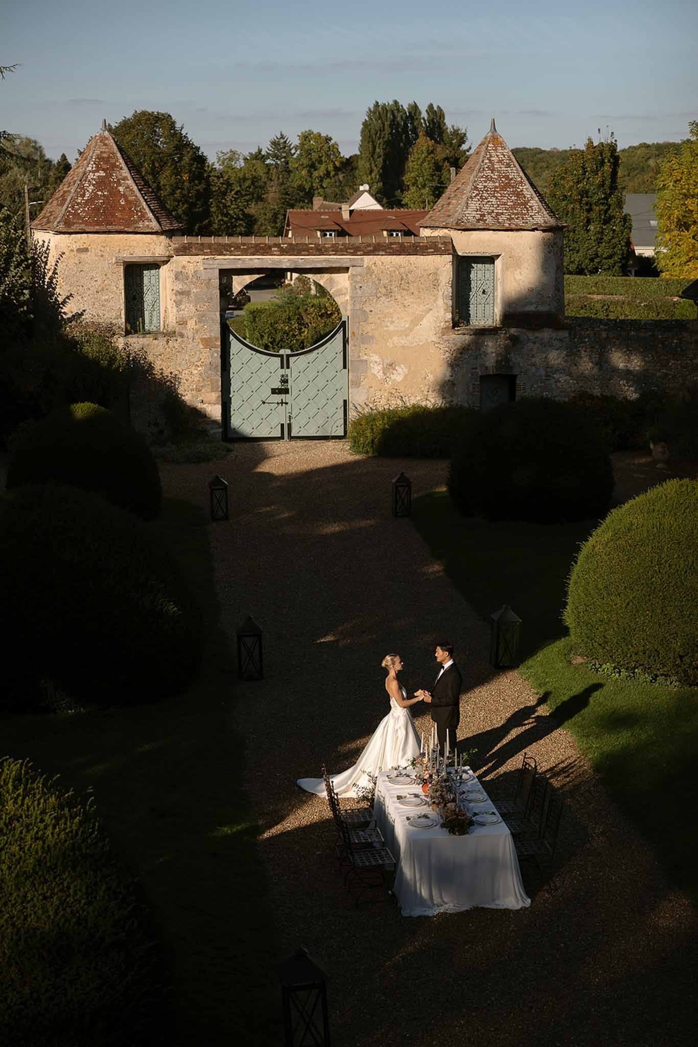 Aerial view of bride and groom holding hands beside candlelit table in chateau courtyard with stone turrets