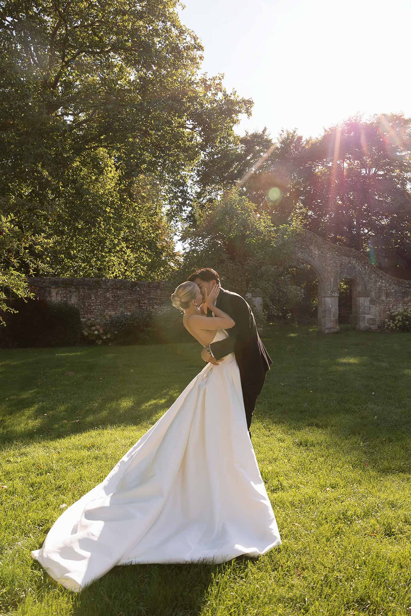 Bride and groom kissing on chateau lawn at golden hour with Gothic stone archway behind