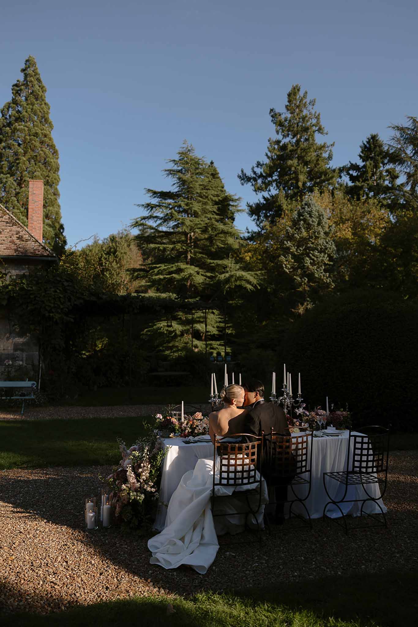 Bride and groom kissing at sweetheart table with mauve floral runner and candelabras at golden hour
