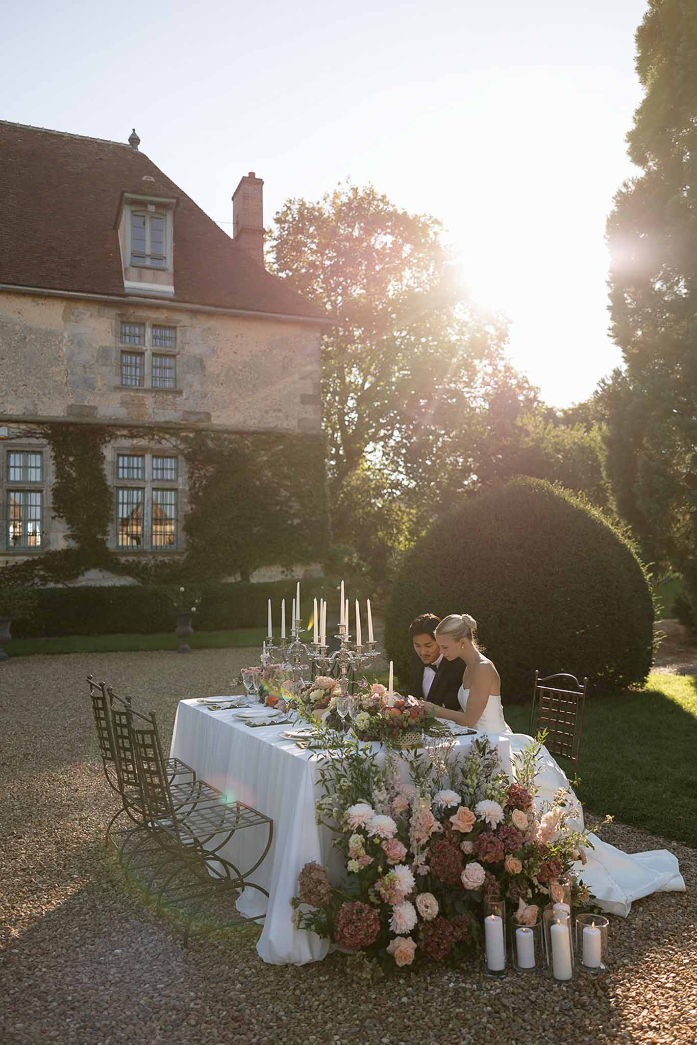 Bride and groom at sweetheart table with blush and burgundy florals and crystal candelabra at golden hour