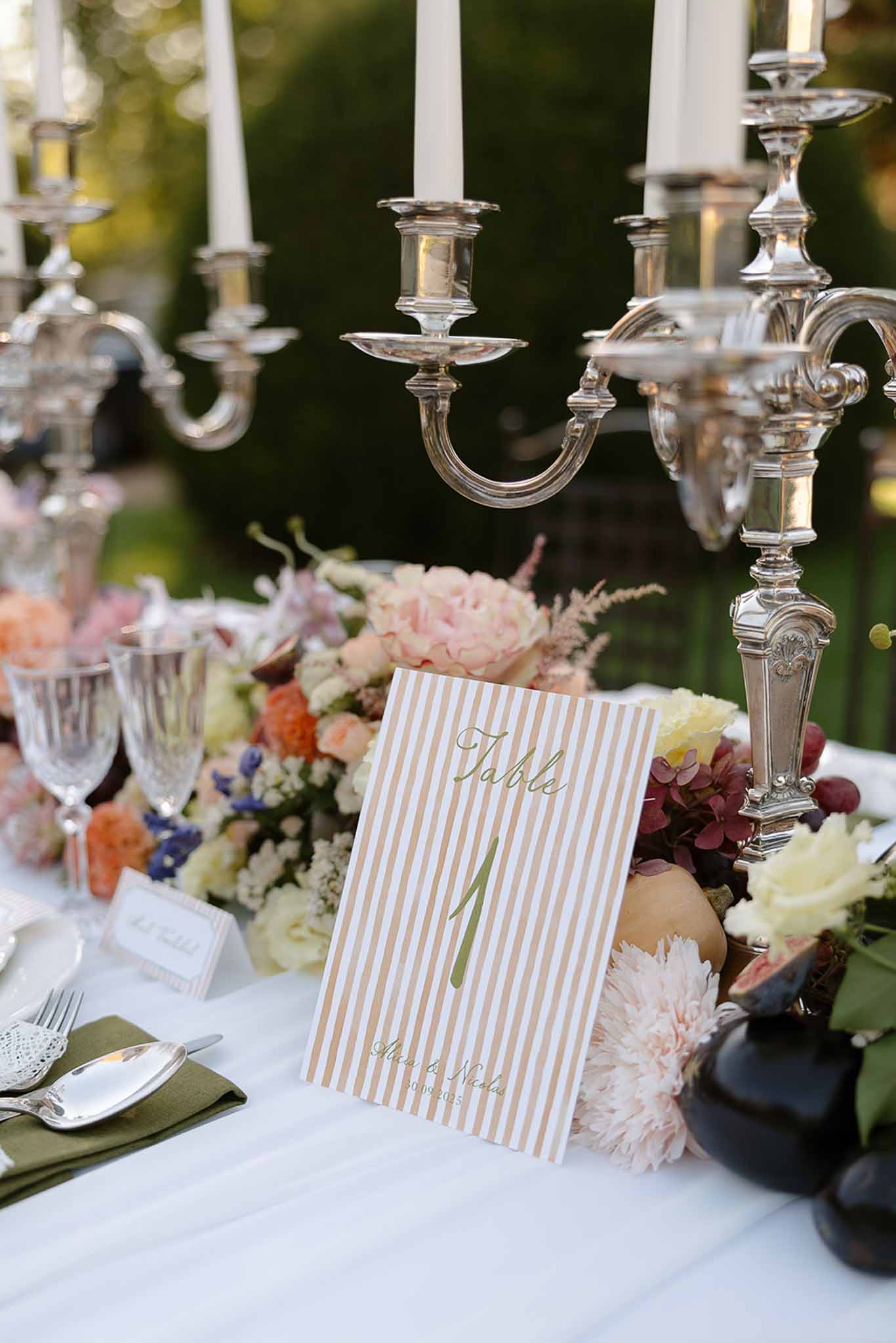 Reception table centerpiece with blush peonies, coral blooms, figs, silver candelabras, and olive green napkins