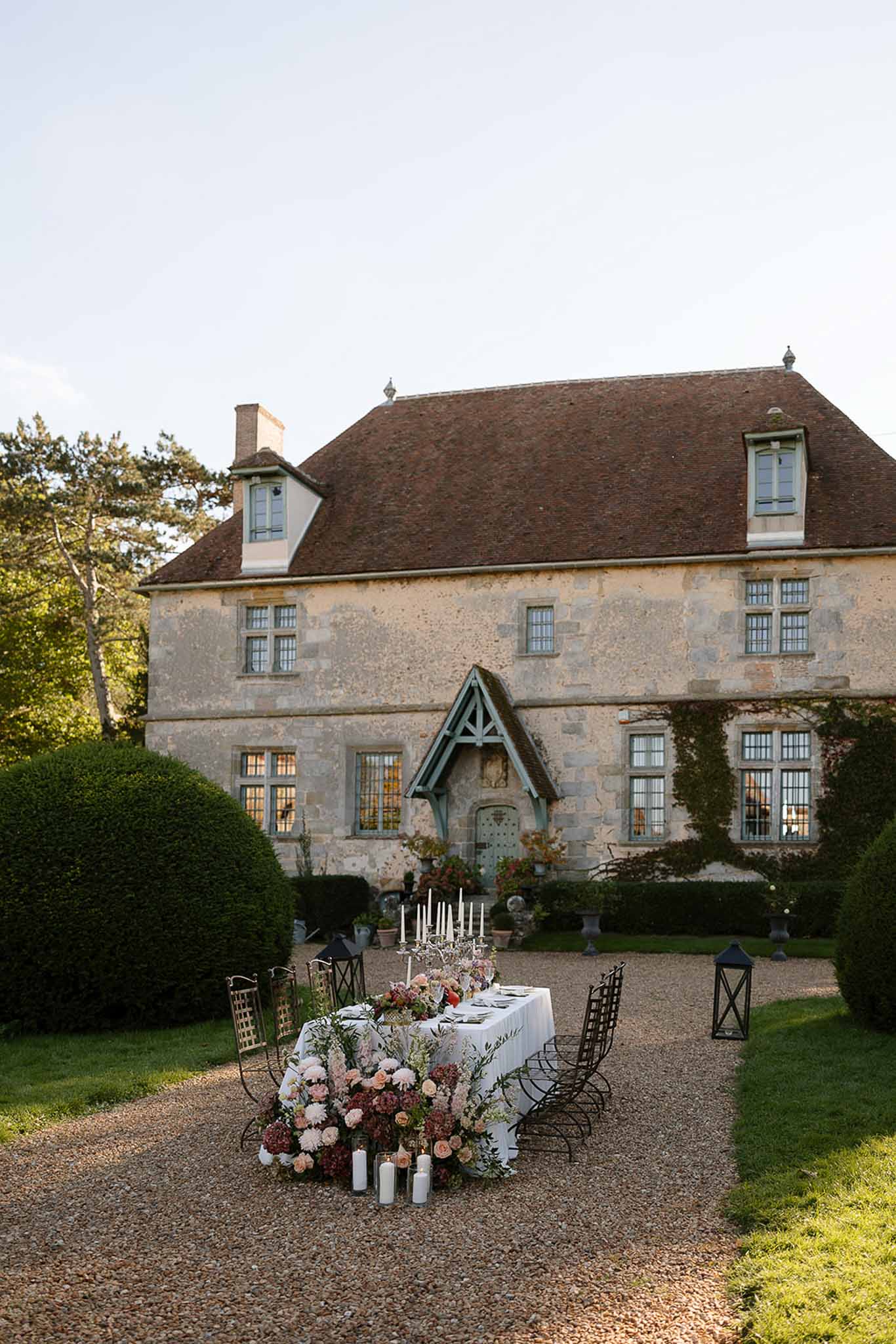 Reception table with cascading blush and burgundy florals, taper candles, and manor facade