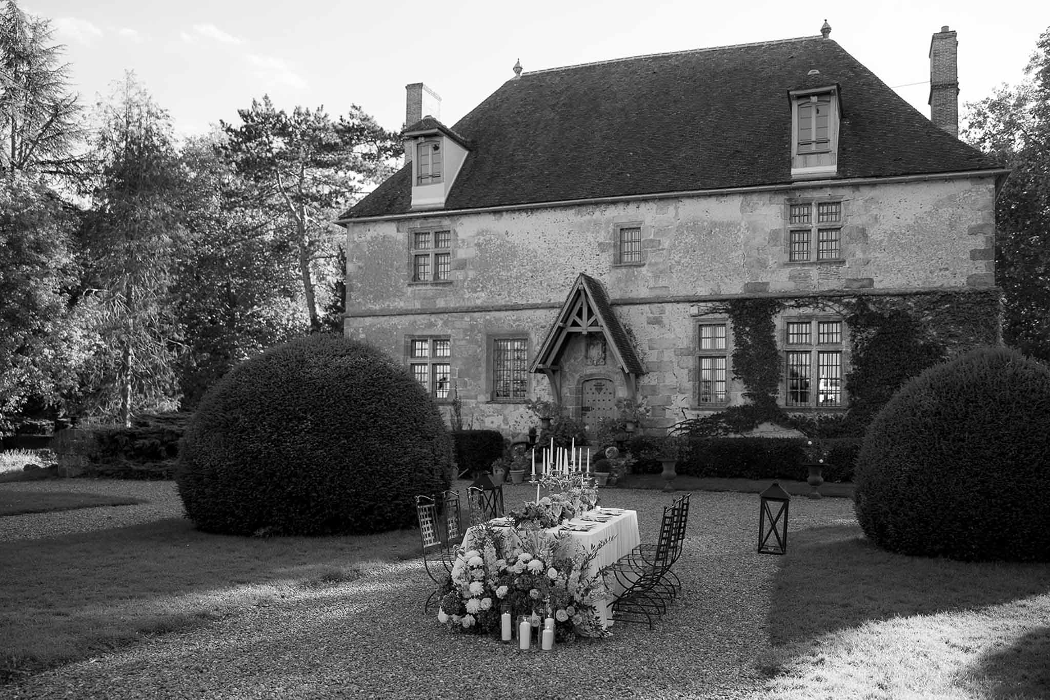 Feasting table with abundant dahlia runner and pillar candles before ivy-clad manor house in B&W