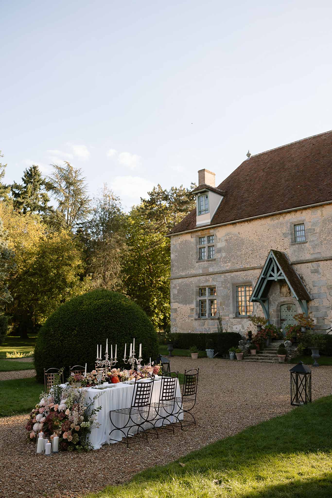 Long table with silver candelabras and cascading blush dahlia arrangements before stone manor with terracotta roof