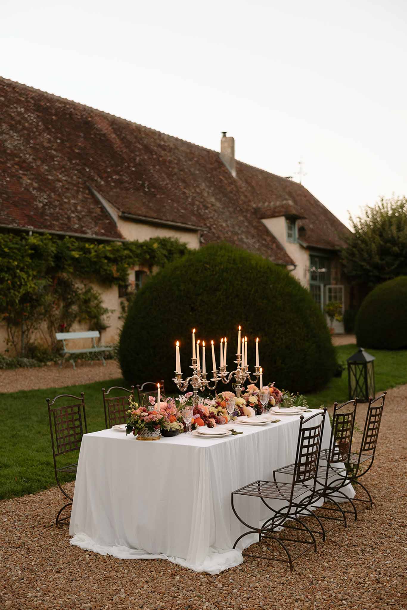 Silver candelabra with coral, blush, and burgundy dahlias on wrought-iron chair table at dusk courtyard