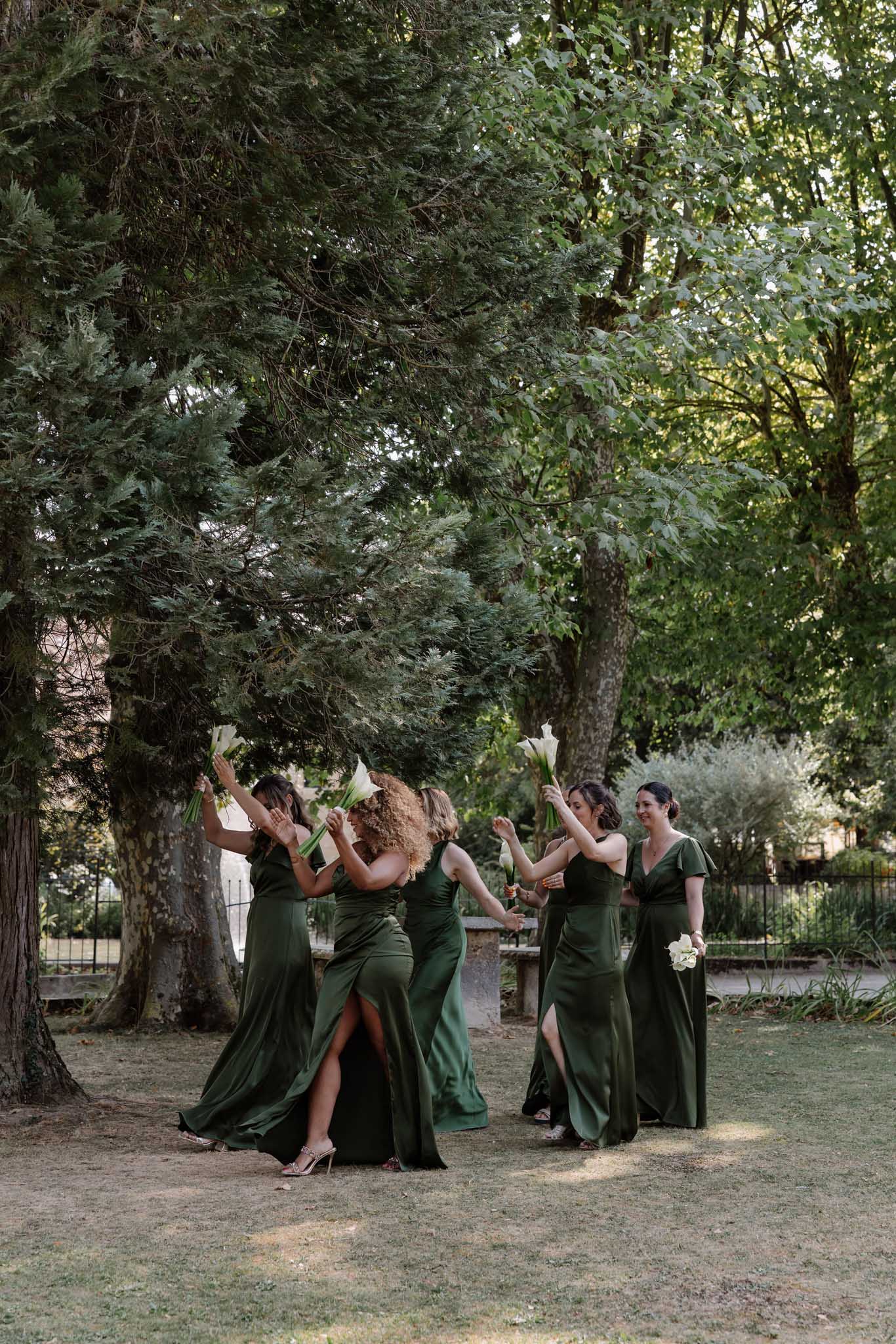Five bridesmaids in forest green satin dresses dancing and raising white calla lily bouquets