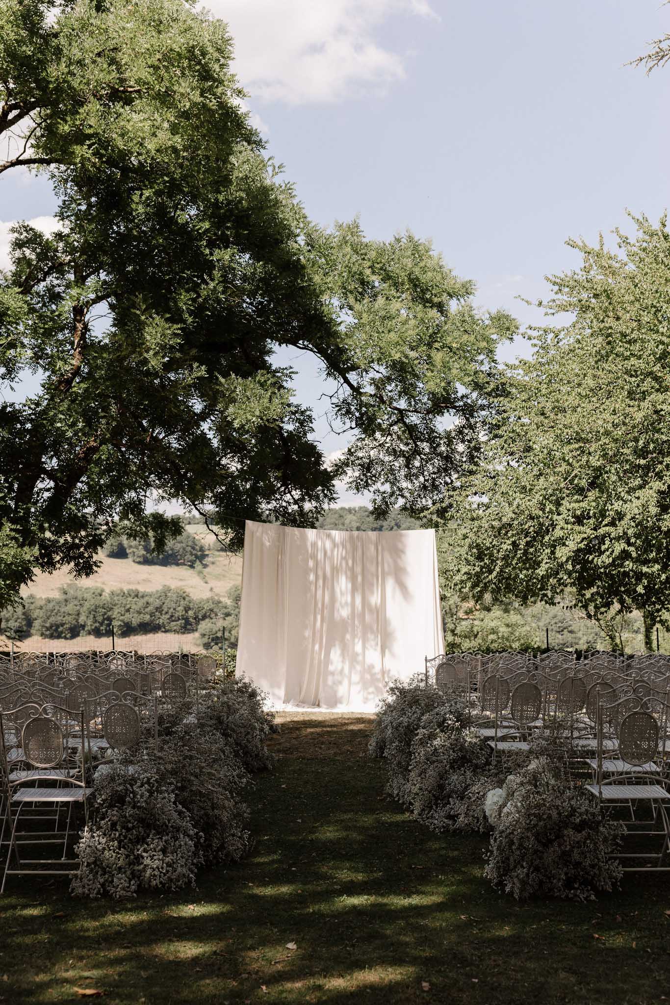 White garden chairs with baby's breath aisle mounds and draped fabric altar curtain on rolling lawn
