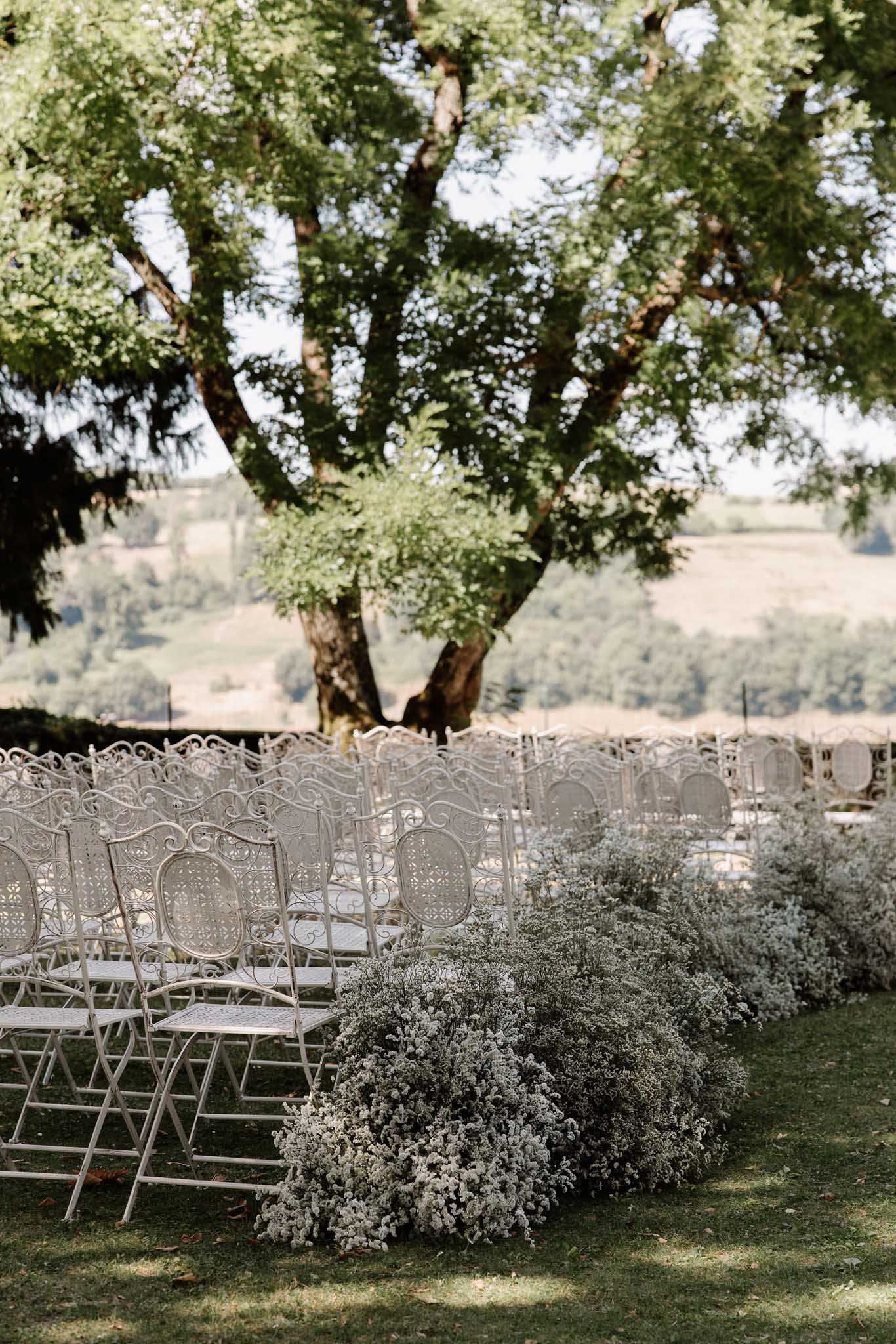 White wrought-iron ceremony chairs on lawn with baby's breath aisle borders and countryside backdrop