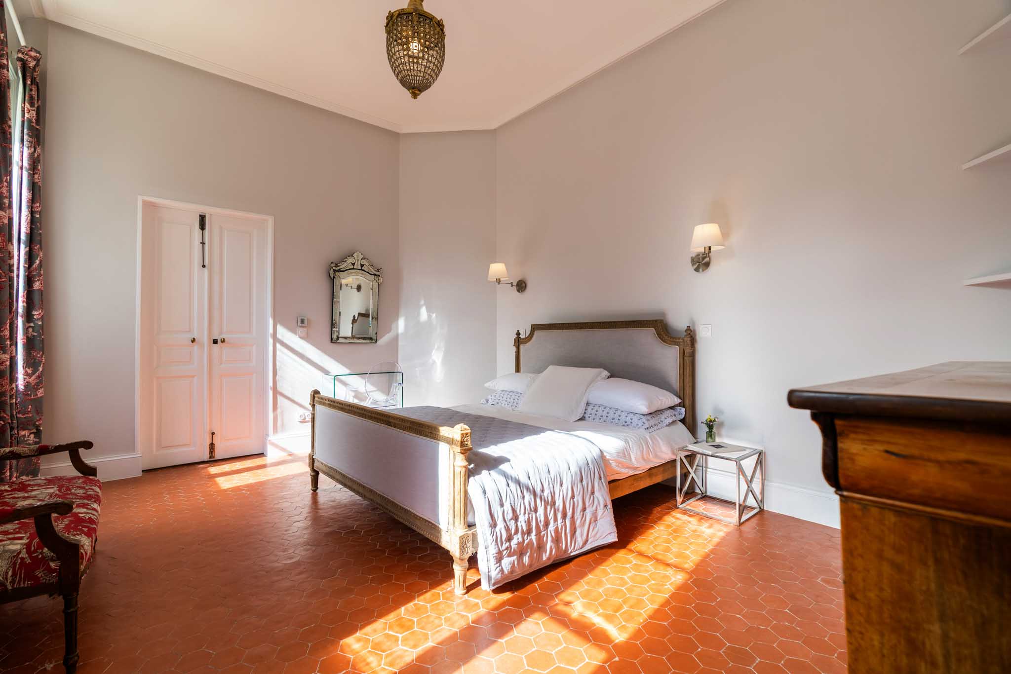 Chateau bedroom with terracotta tiles carved Louis XVI bed gold chandelier and red toile chair