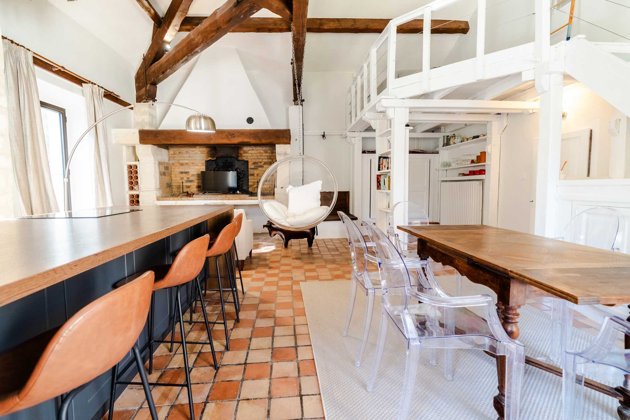 Renovated French country interior with exposed beams, terracotta floors, rustic dining table and hanging bubble chair