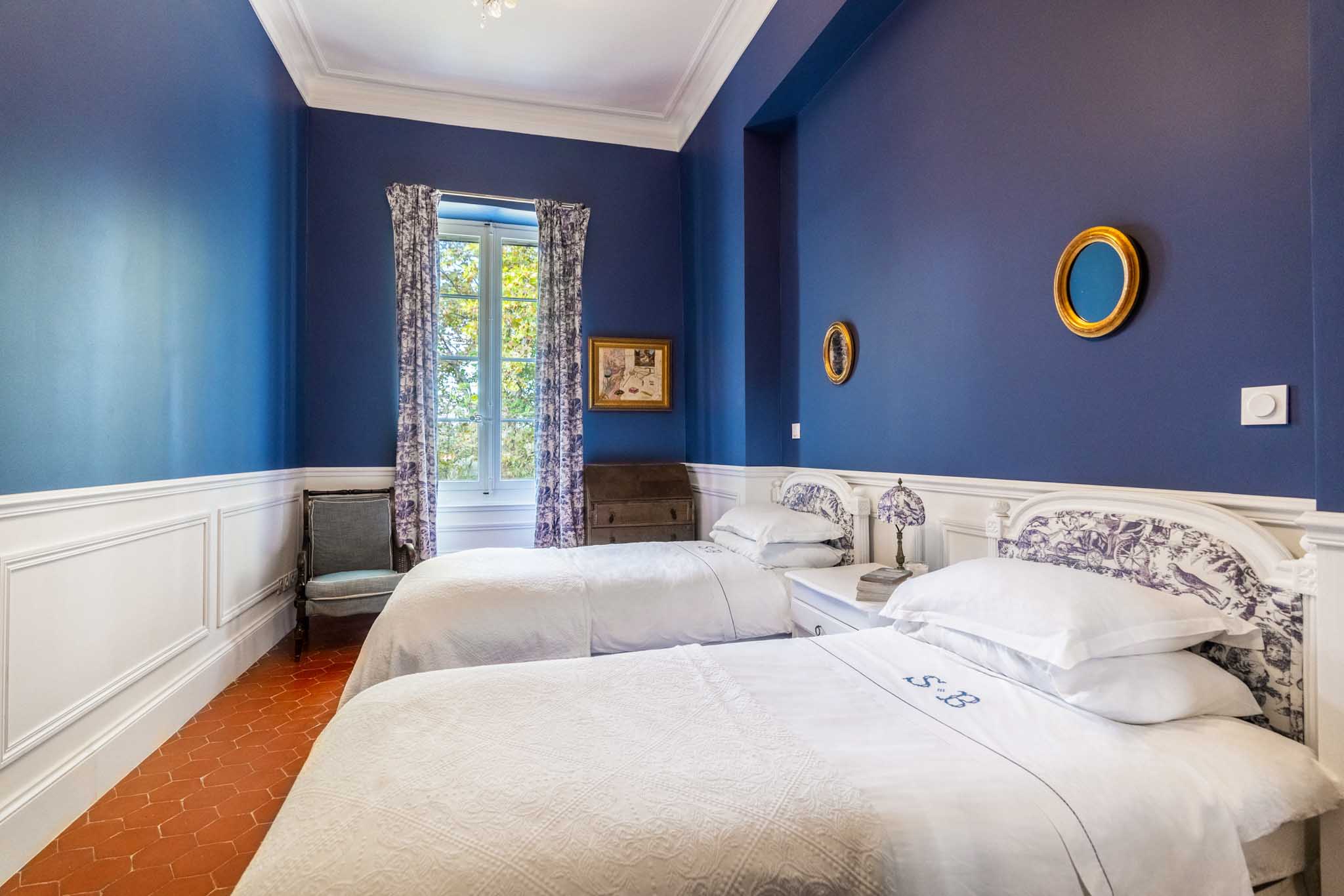 French chateau guest bedroom with cobalt blue walls, white wainscoting, toile de Jouy fabric, and twin beds
