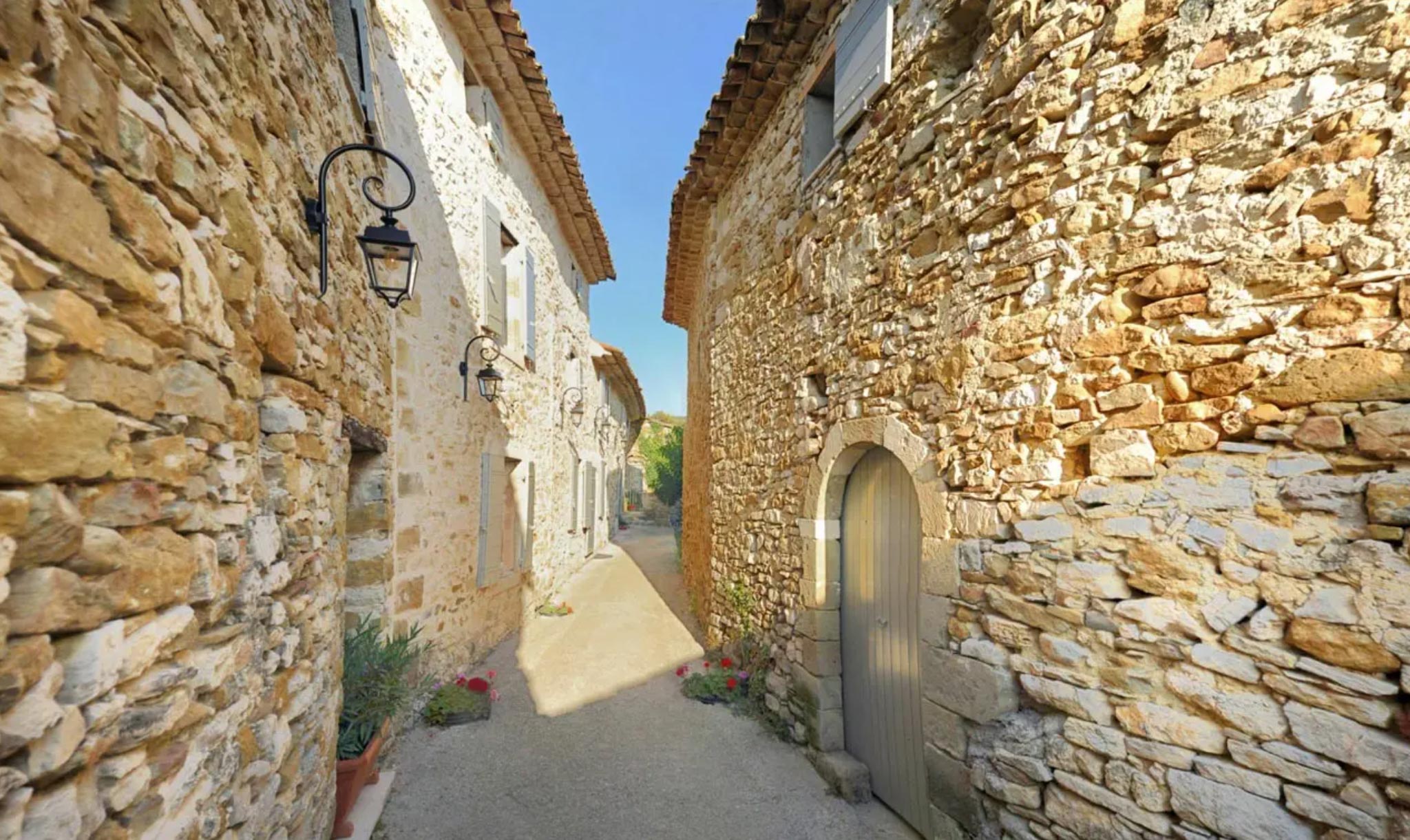 Narrow stone alleyway between Provencal buildings with wrought-iron lanterns, shuttered windows, and potted plants