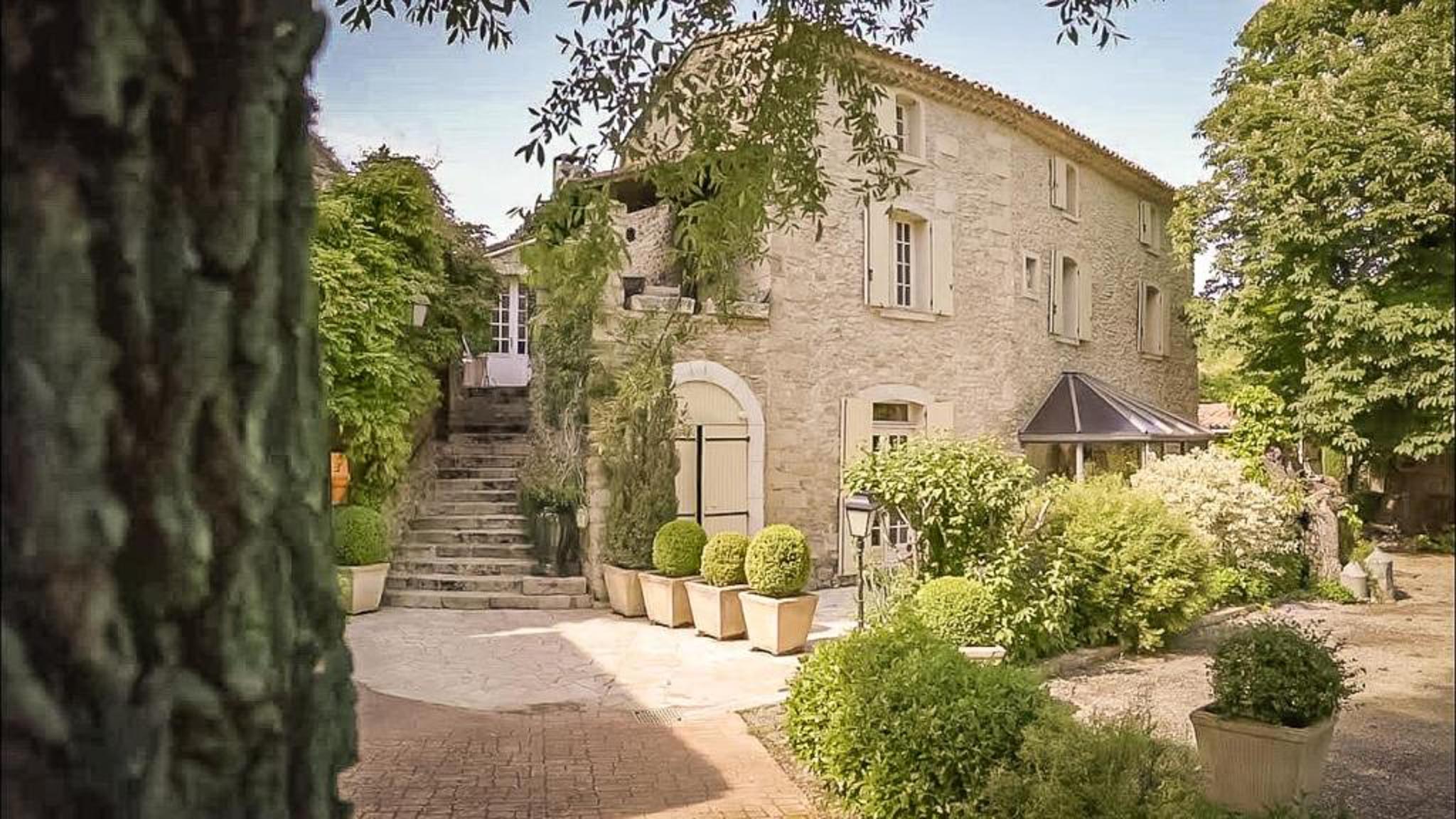 Provencal stone mas with cream shutters, arched doorways, boxwood topiary, and exterior stone staircase