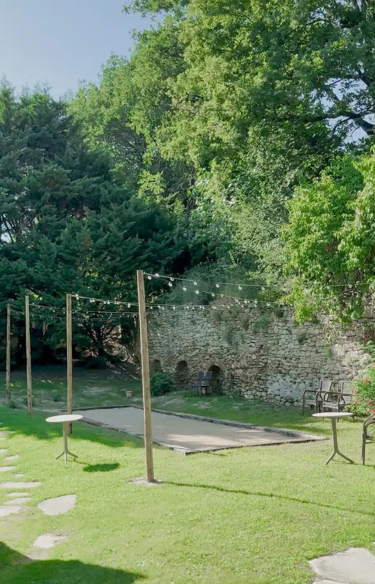 Petanque court with globe fairy lights between tall posts in walled garden with stone arched alcoves