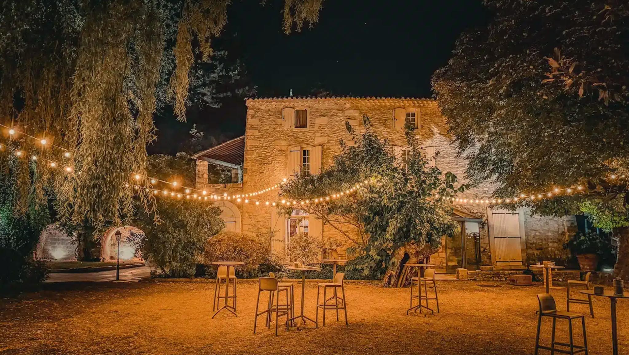 Nighttime Provencal mas courtyard with bistro string lights high cocktail tables and golden limestone walls