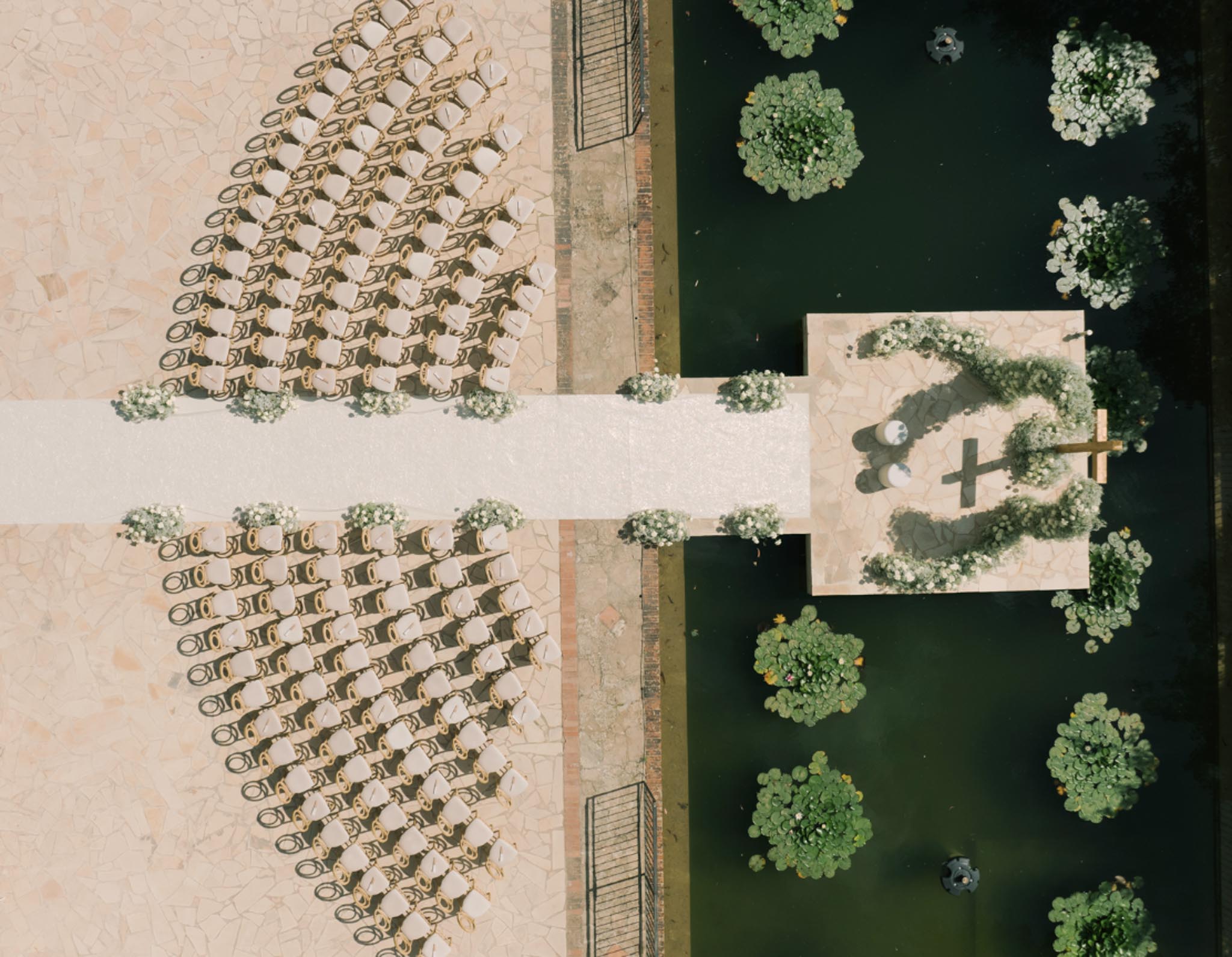 Aerial ceremony on terracotta terrace with 100 gold chairs, white aisle runner, and circular floral arch