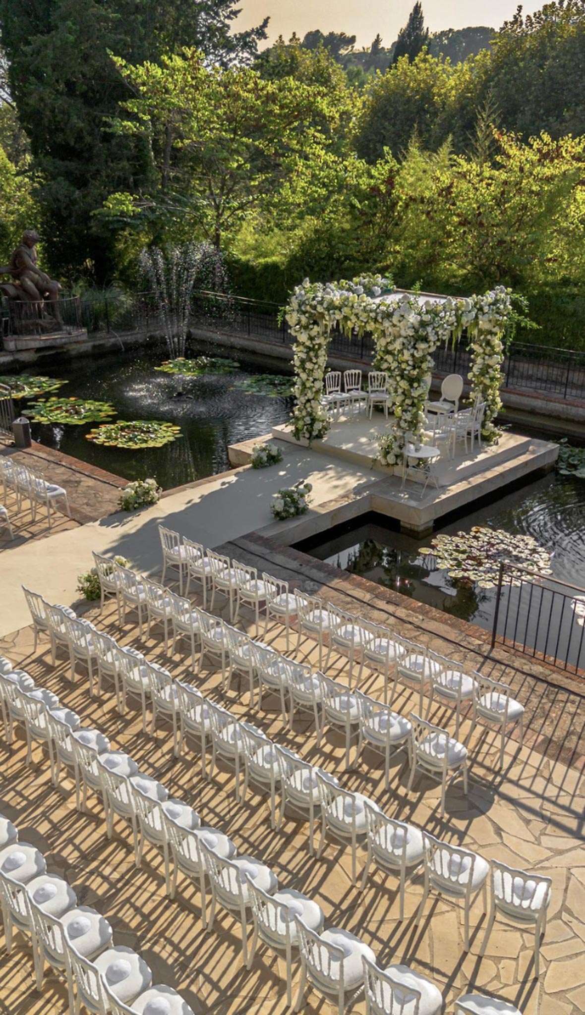 Aerial view of outdoor ceremony setup over lily pond with square floral arch and white chair rows