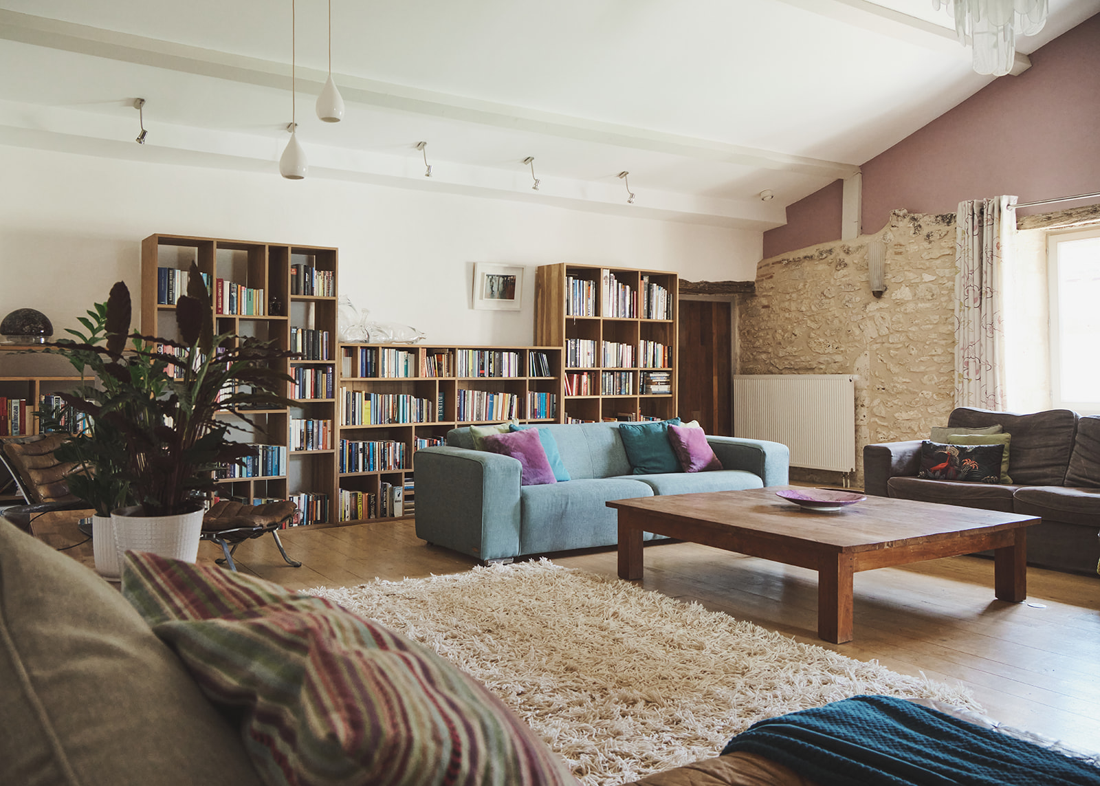 Eclectic living room with exposed limestone wall oak bookcases blue sofa and leather armchairs