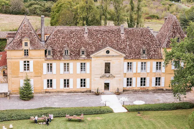 Aerial view of French chateau with ochre limestone walls, white shutters, and terracotta mansard roof