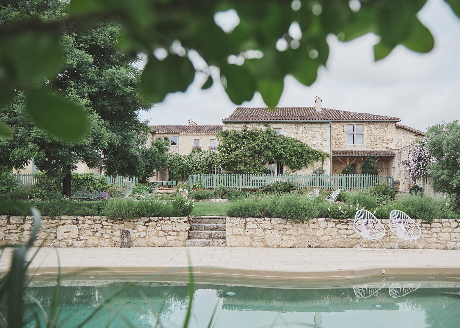 Honey-toned stone mas with pool, Acapulco chairs, and tiered garden viewed through soft foliage