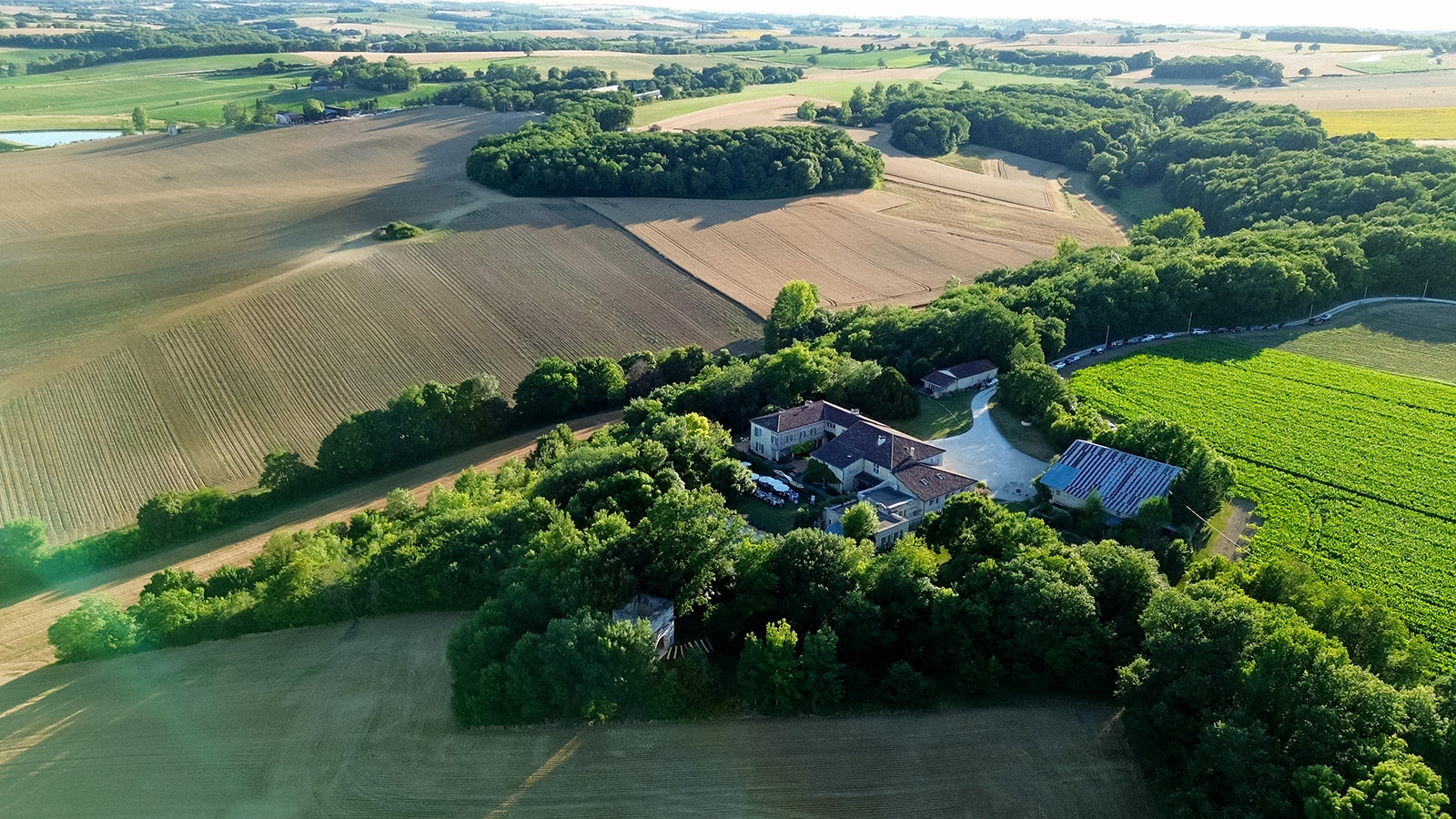 Aerial view of French country estate with stone buildings and vineyard amid agricultural fields