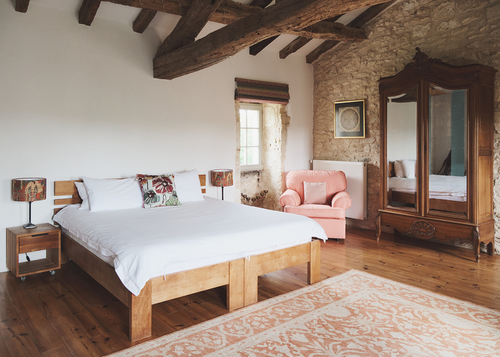 French chateau guest bedroom with oak bed, antique walnut armoire, exposed stone walls, and wooden ceiling beams