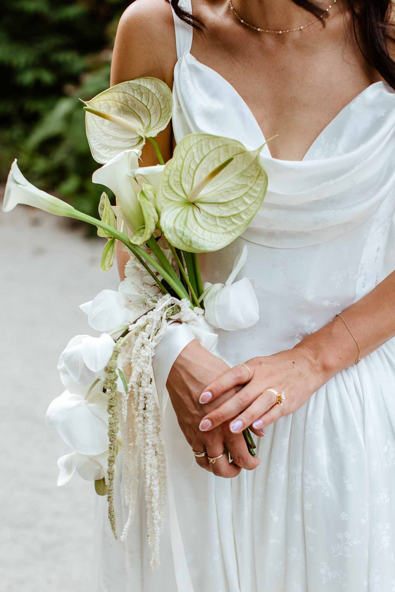 Bride holding sculptural white anthurium, calla lily, and orchid bouquet with satin ribbon in cowl-neck gown