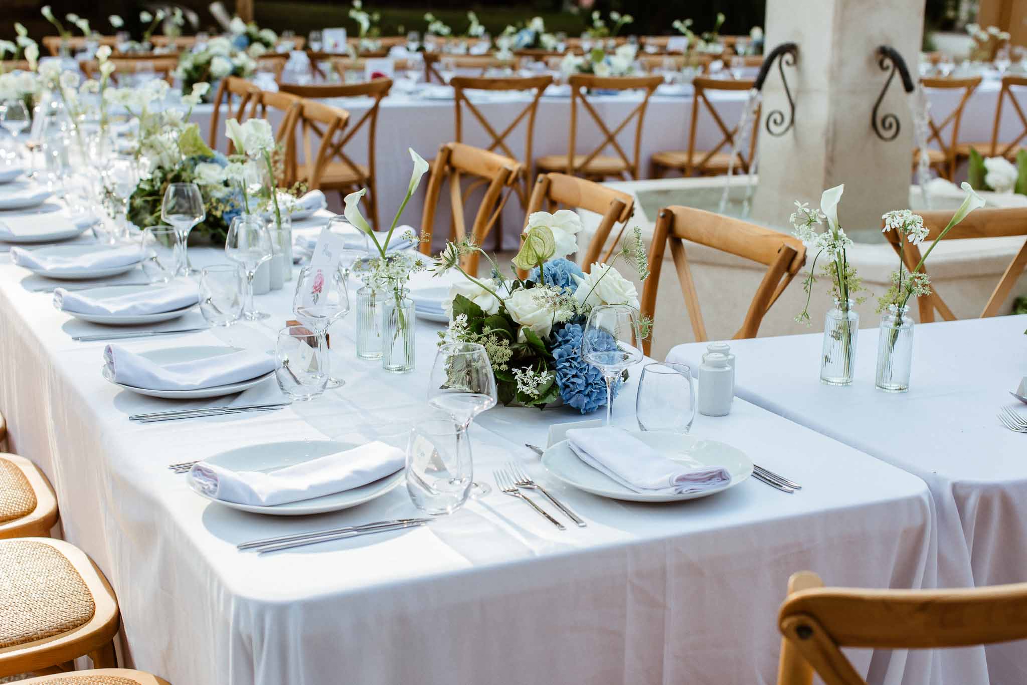 Reception tablescape with dusty blue hydrangeas, white calla lilies, bud vases, and white plate settings