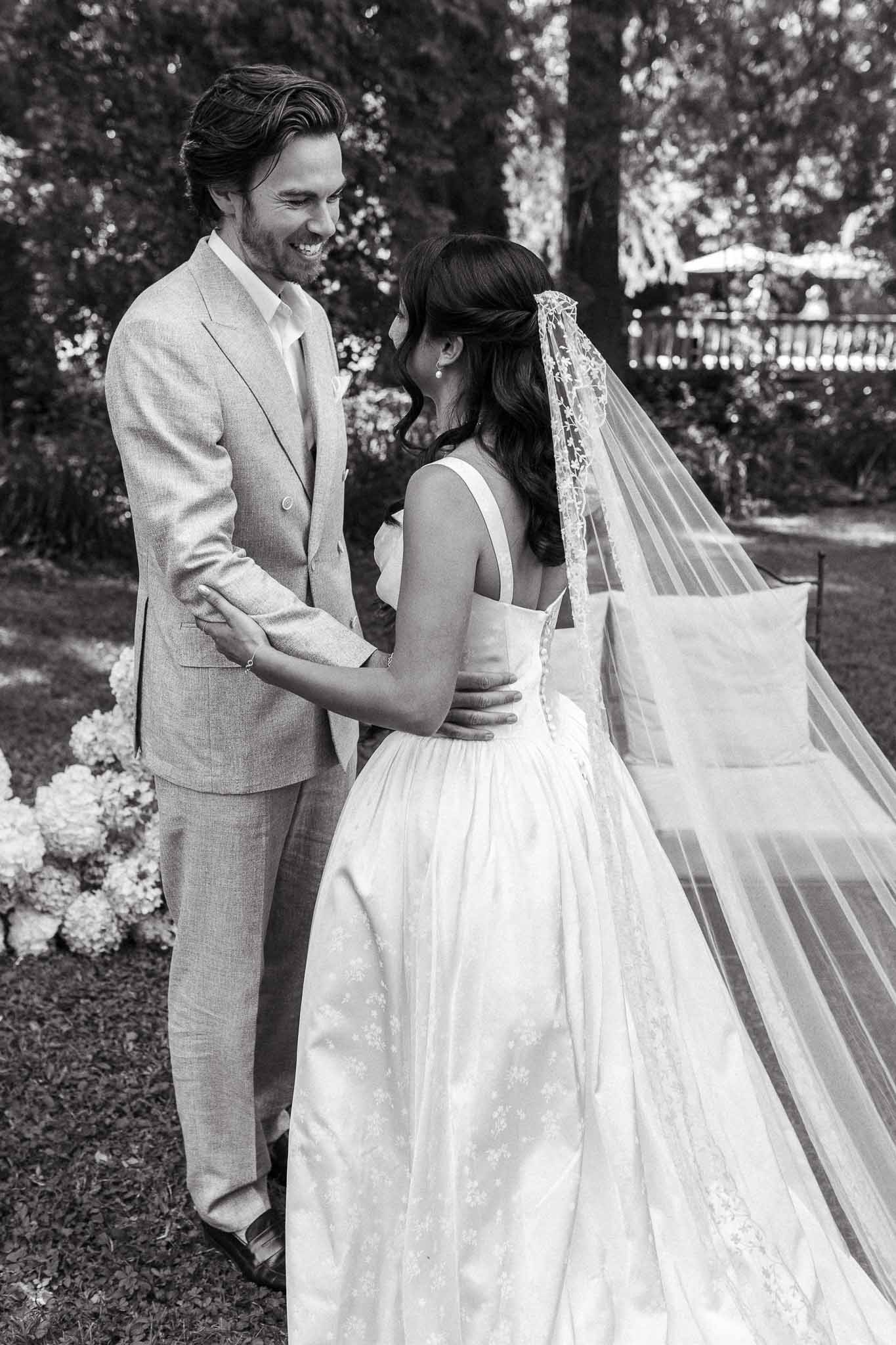 Bride and groom embracing in garden with bride's embroidered ball gown and lace cathedral veil in black and white