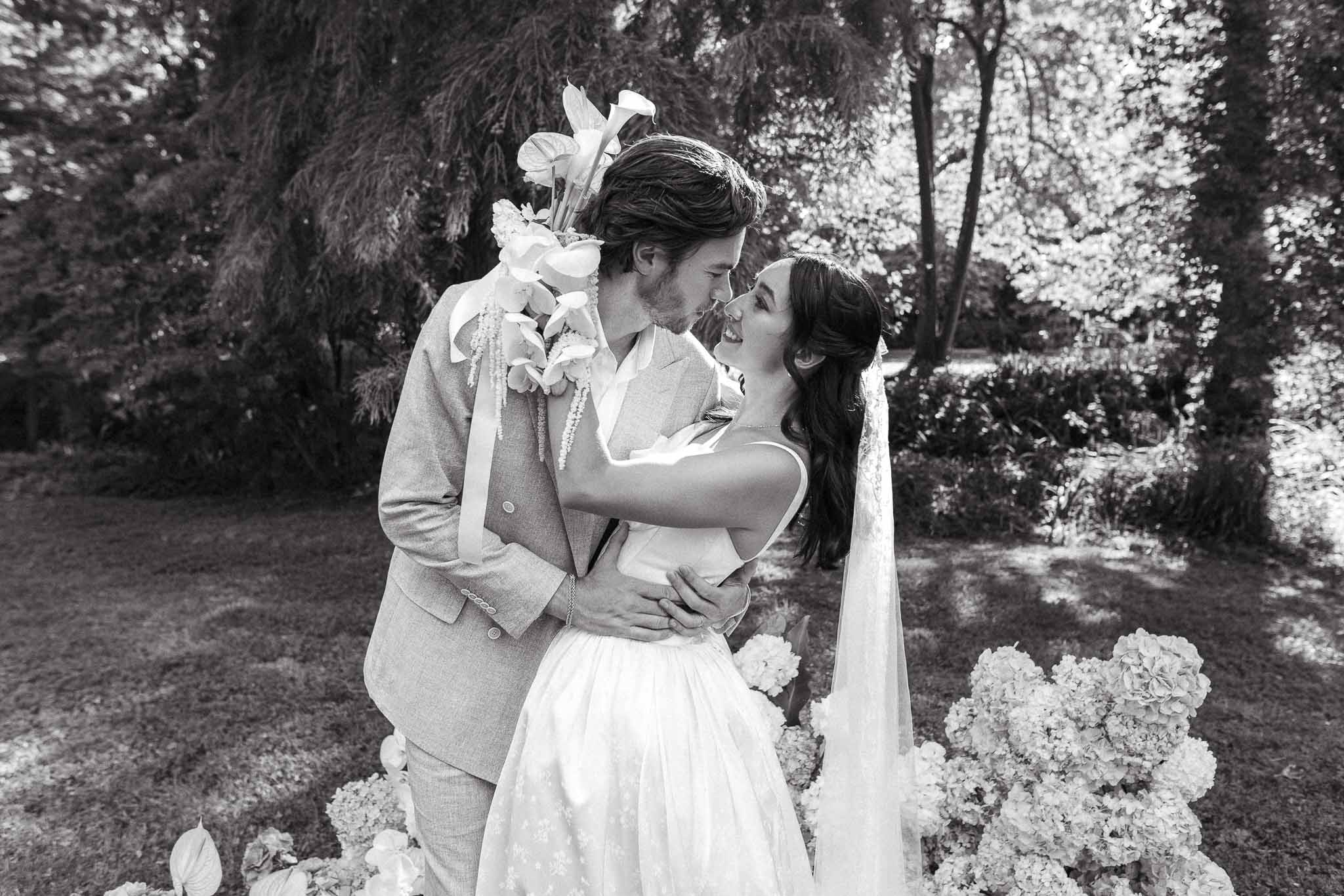 Black and white couple kissing in garden with sculptural calla lily bouquet and hydrangea ground clusters