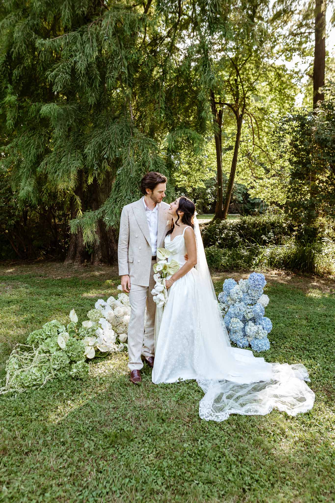 Couple between green anthurium ground installation and blue hydrangea column with orchid bouquet