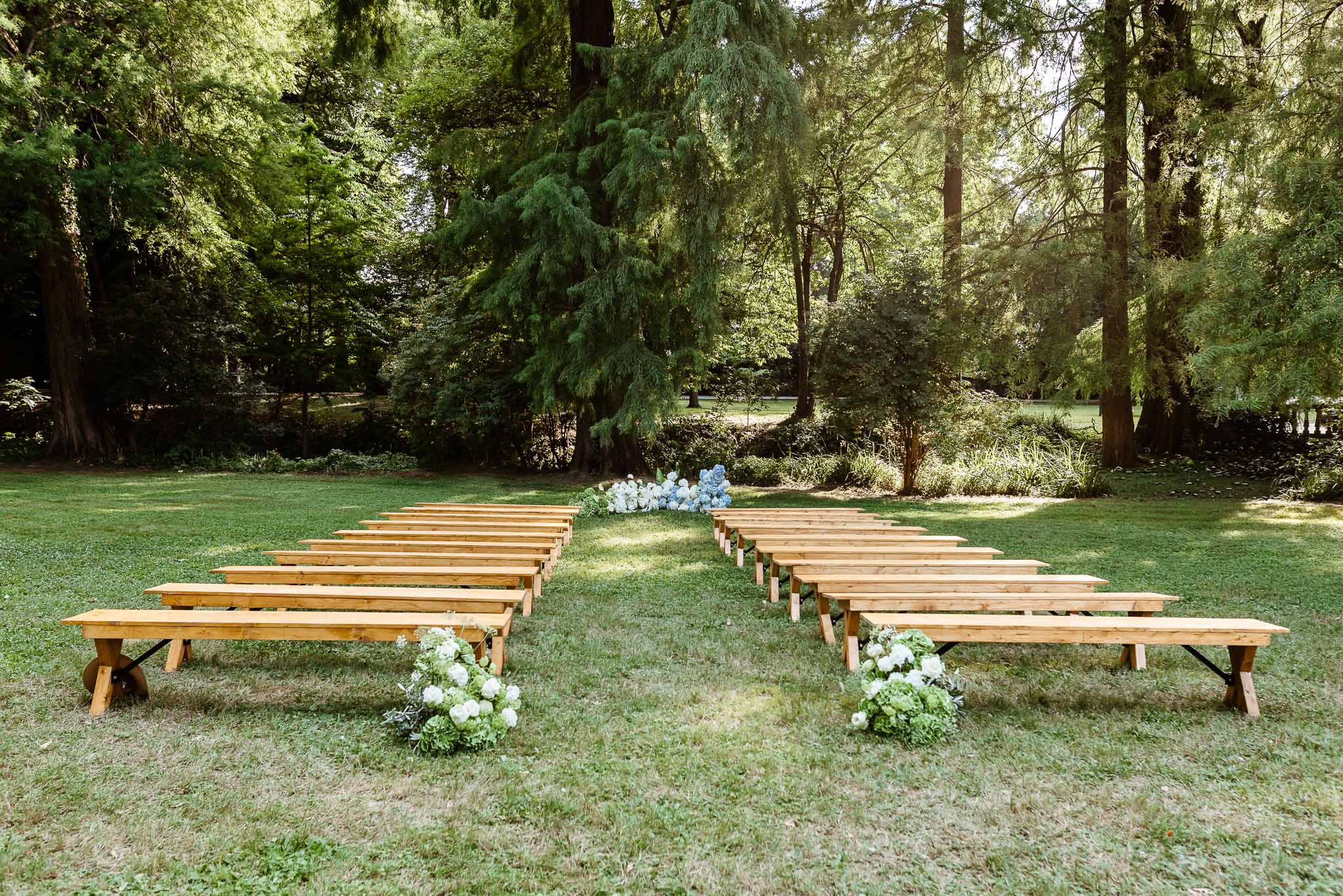 Wooden bench ceremony setup on lawn with white peony aisle markers and blue hydrangea altar