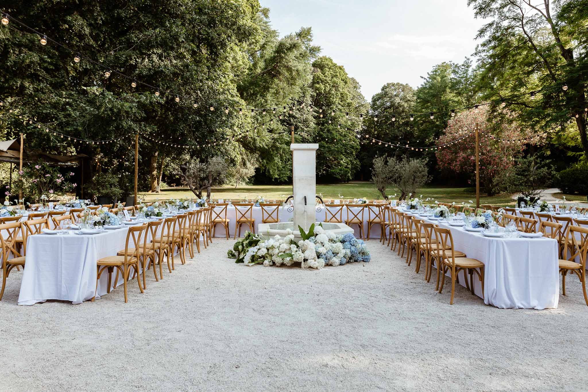 Outdoor courtyard reception with round and long tables around stone fountain, string lights overhead