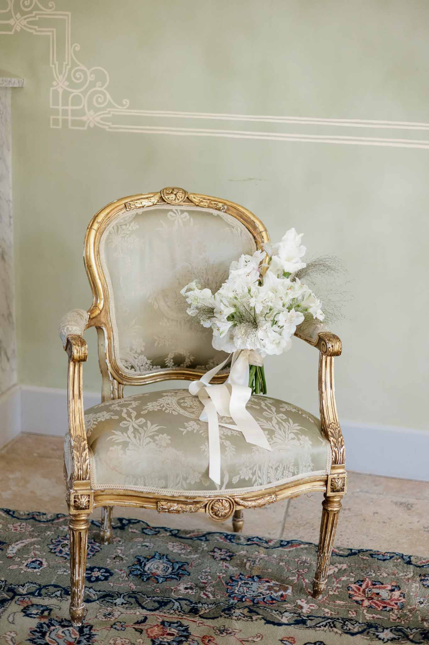 White sweet pea and hydrangea bouquet with ivory ribbons on gilt Louis XVI chair in sage chateau room