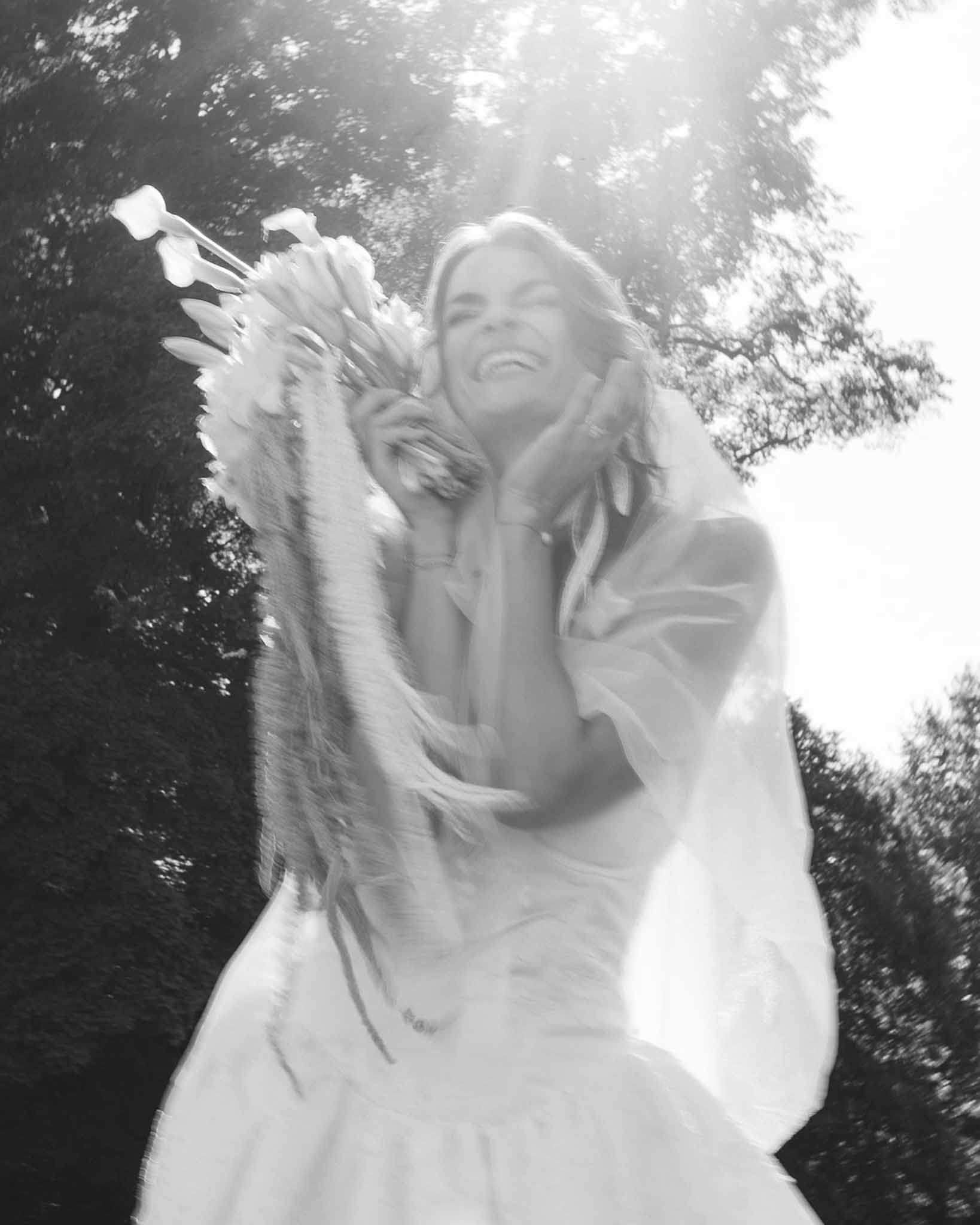 Bride laughing outdoors holding calla lily and pampas grass bouquet with motion blur in B&W