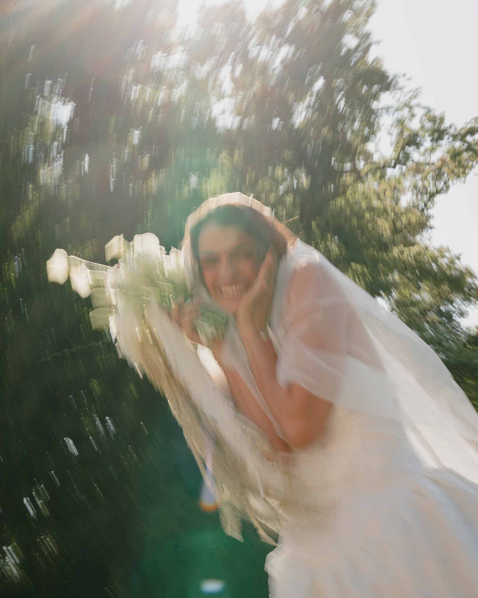 Motion-blurred artistic portrait of smiling bride with cathedral veil and lens flare in garden setting