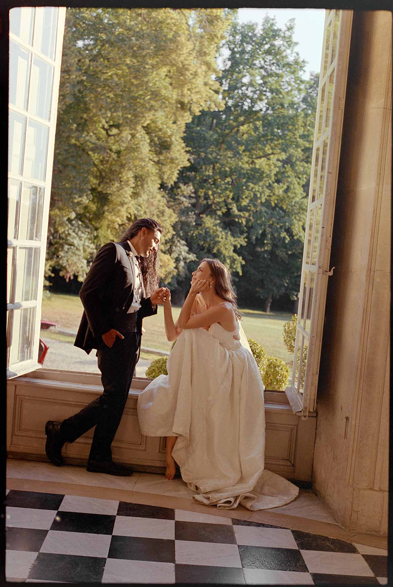 Bride and groom in chateau doorway with checkered marble floor and golden light from garden