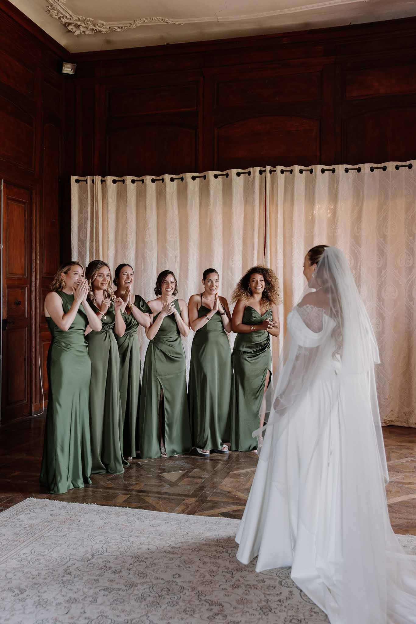 Bride in white off-shoulder gown with cathedral veil revealed to five bridesmaids in olive satin dresses