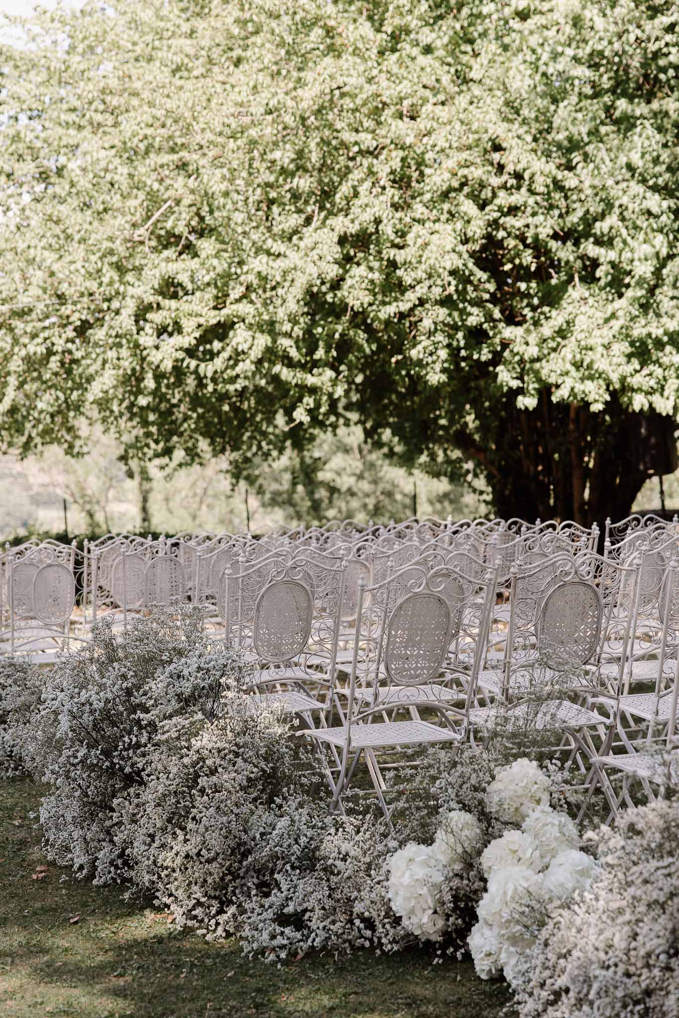 White wrought-iron ceremony chairs with baby's breath and hydrangea aisle border on lawn