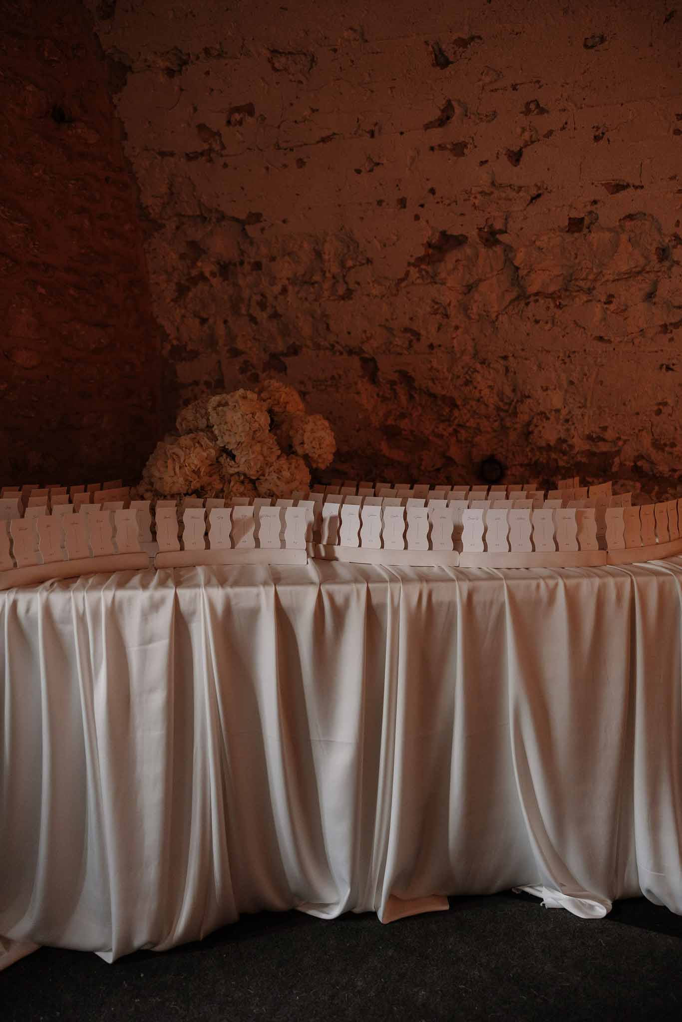 Escort card table with blush place cards and peach hydrangea cluster against stone cellar wall