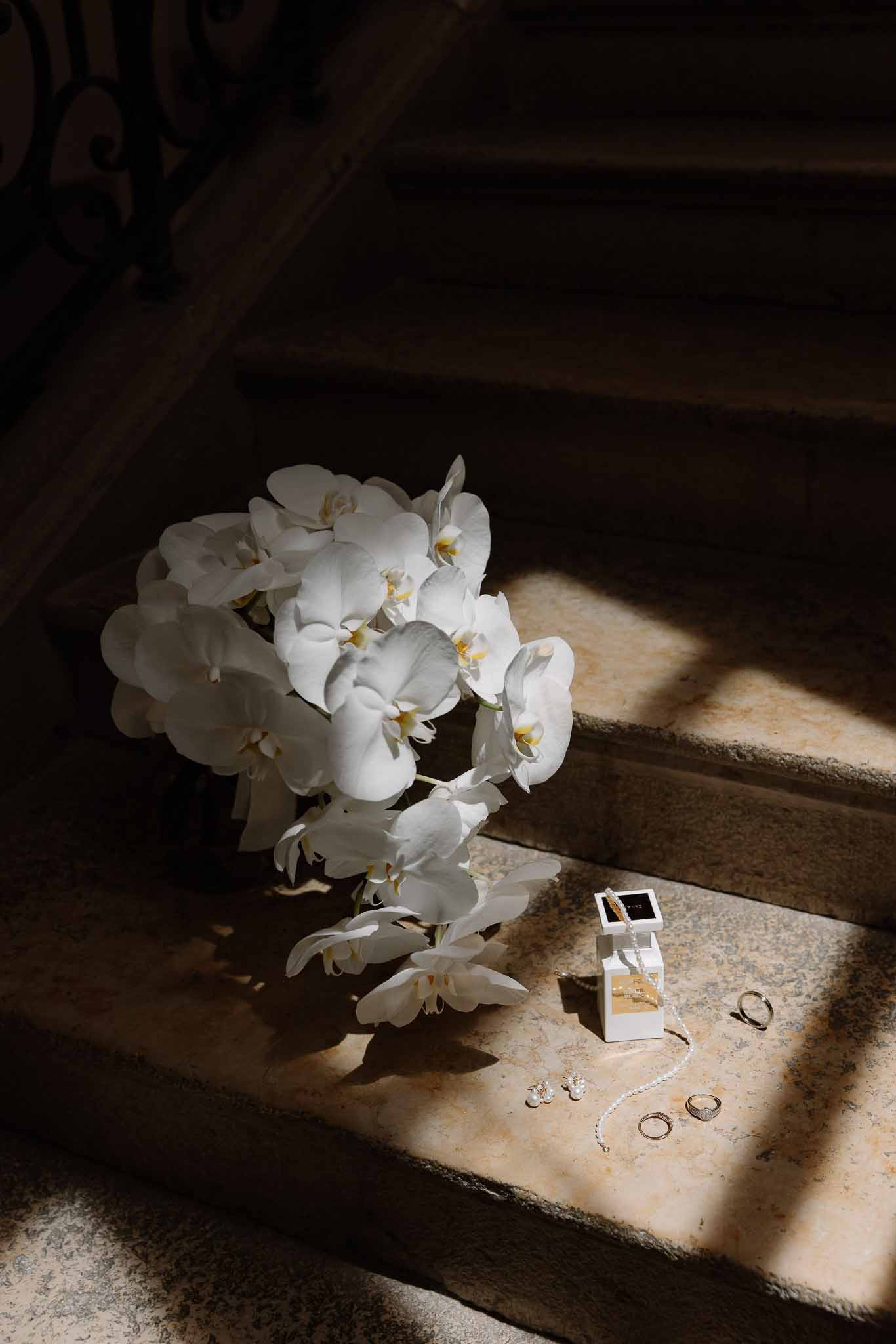 White phalaenopsis orchid bouquet with gold rings, pearl bracelet, and velvet box on stone steps