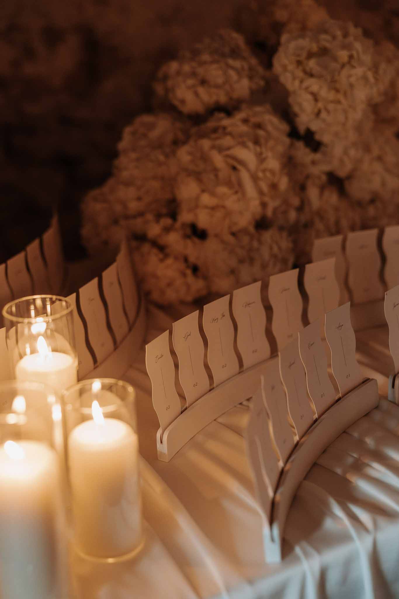 Escort card display with scalloped cream cards, pillar candles in hurricanes, and ivory florals