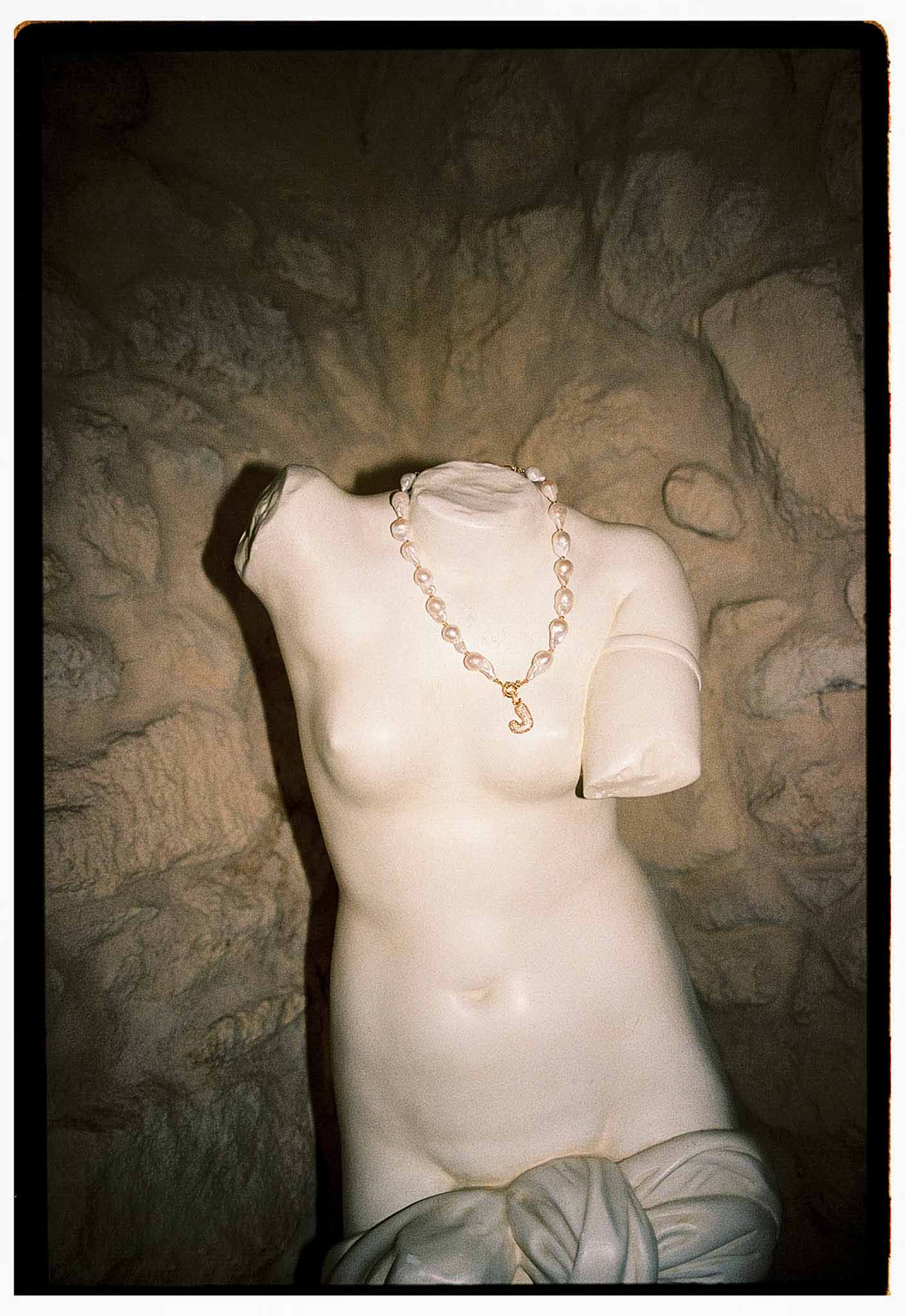 Baroque pearl necklace with gold initial pendant draped on white classical torso sculpture