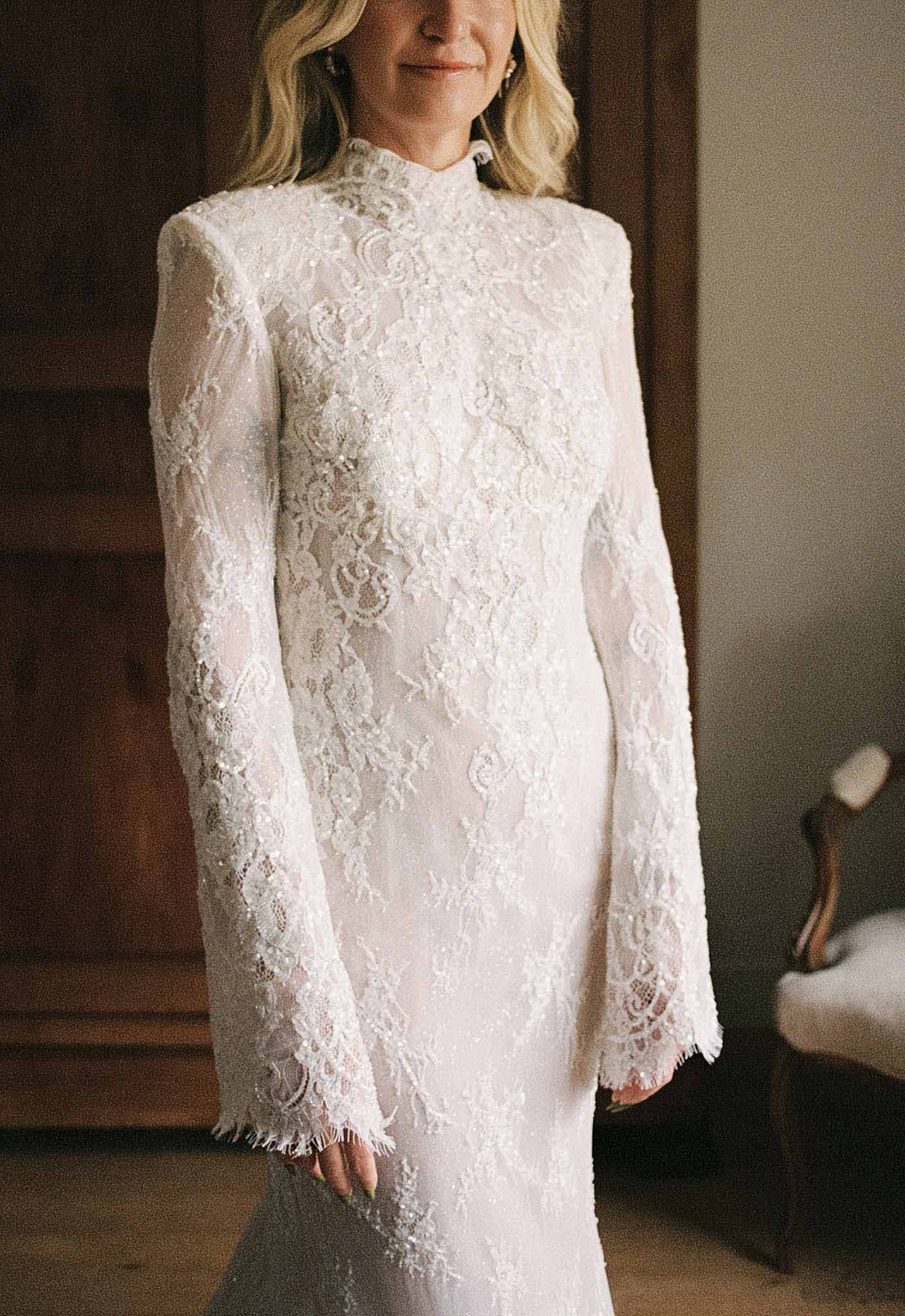 Close-up of beaded lace mock-neck gown with floral applique and fringe sleeve hem detail